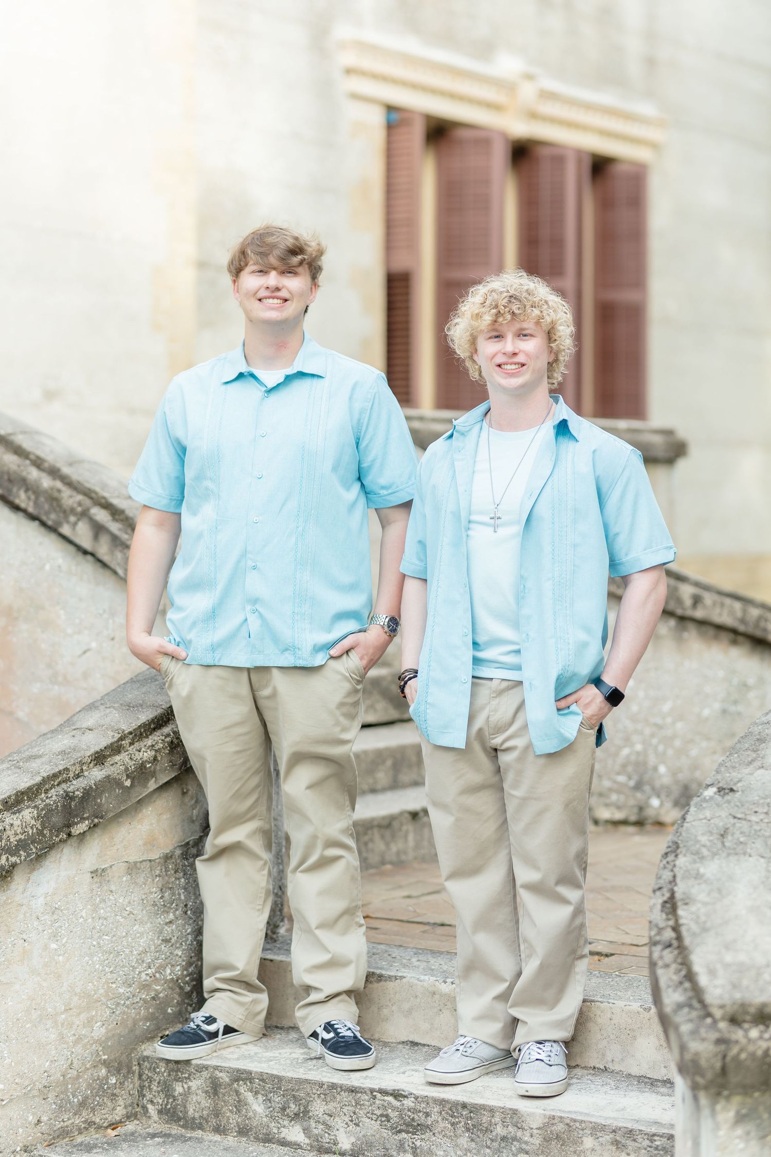 Two people wearing matching light blue shirts and khaki pants stand on stone steps in an outdoor setting.