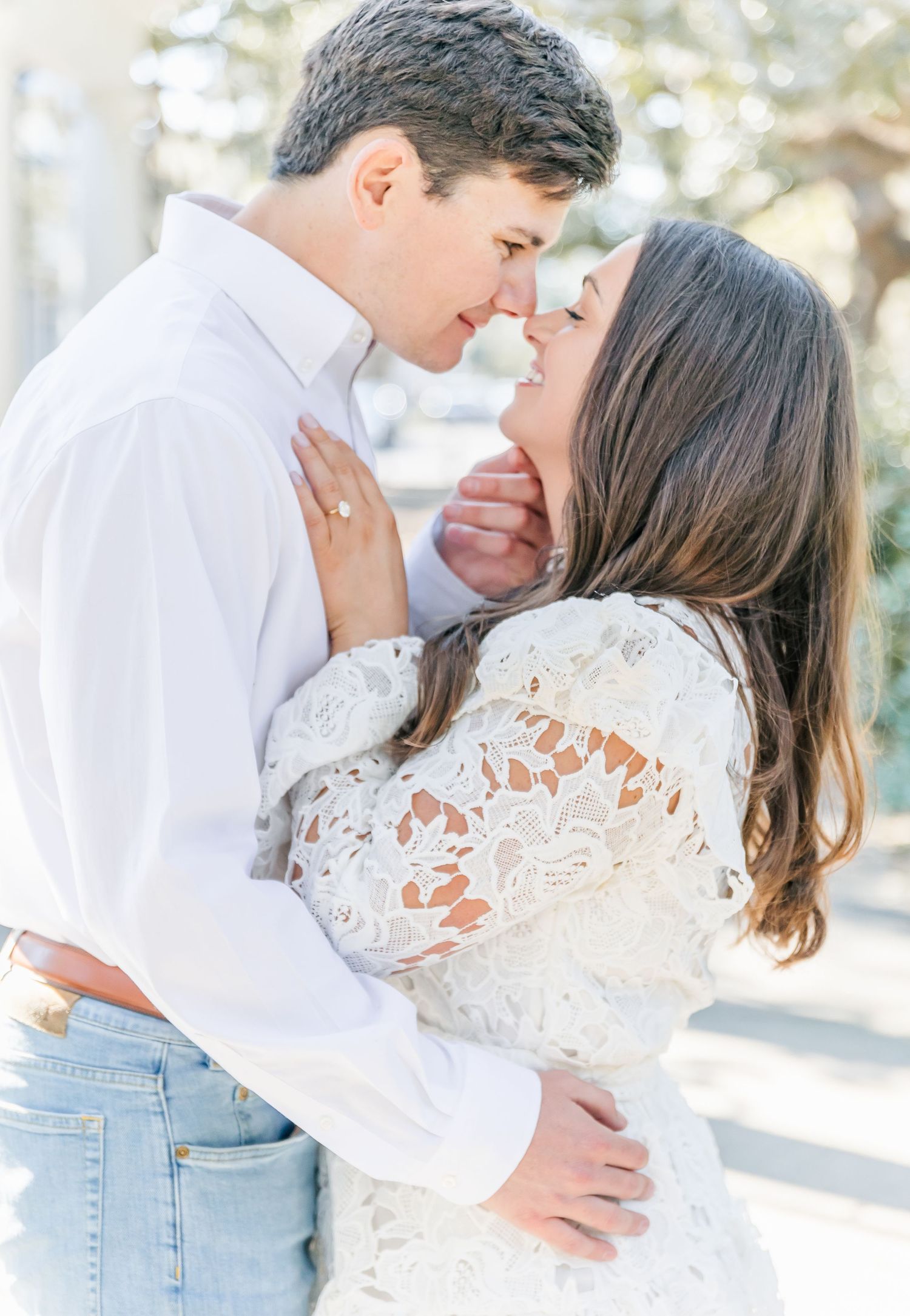 Couple in white and denim sharing an intimate embrace in a sunlit outdoor setting.