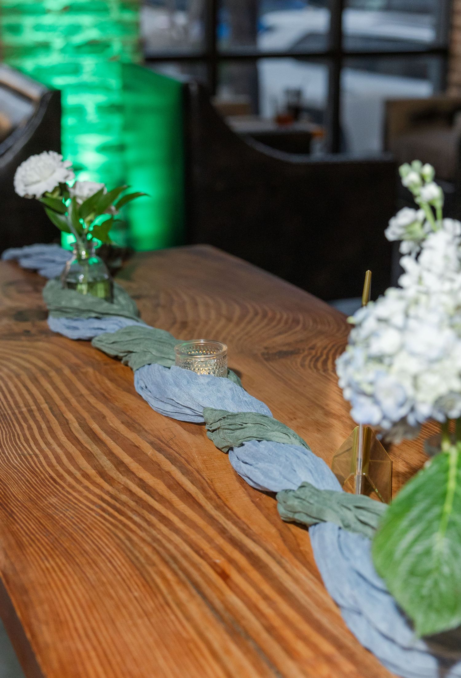 Rustic wooden table with leaf garland runner, white flowers, and glass vases at event.