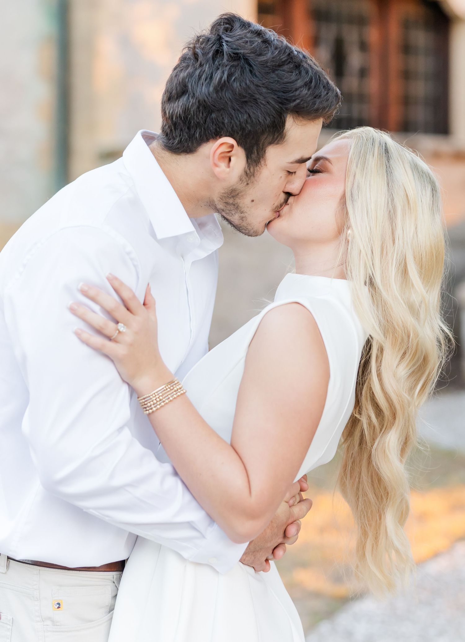 Couple dressed in white embracing and kissing during a romantic outdoor photoshoot.