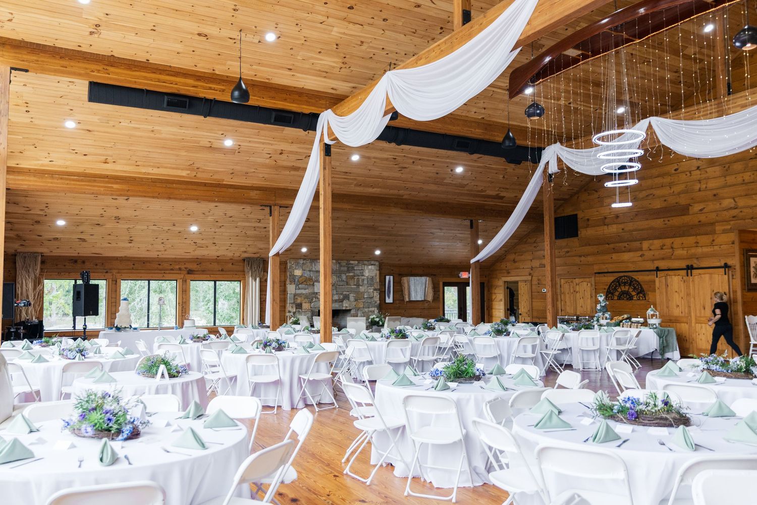 A rustic wooden event venue with white draped ceiling decor and tables set up for a wedding reception.