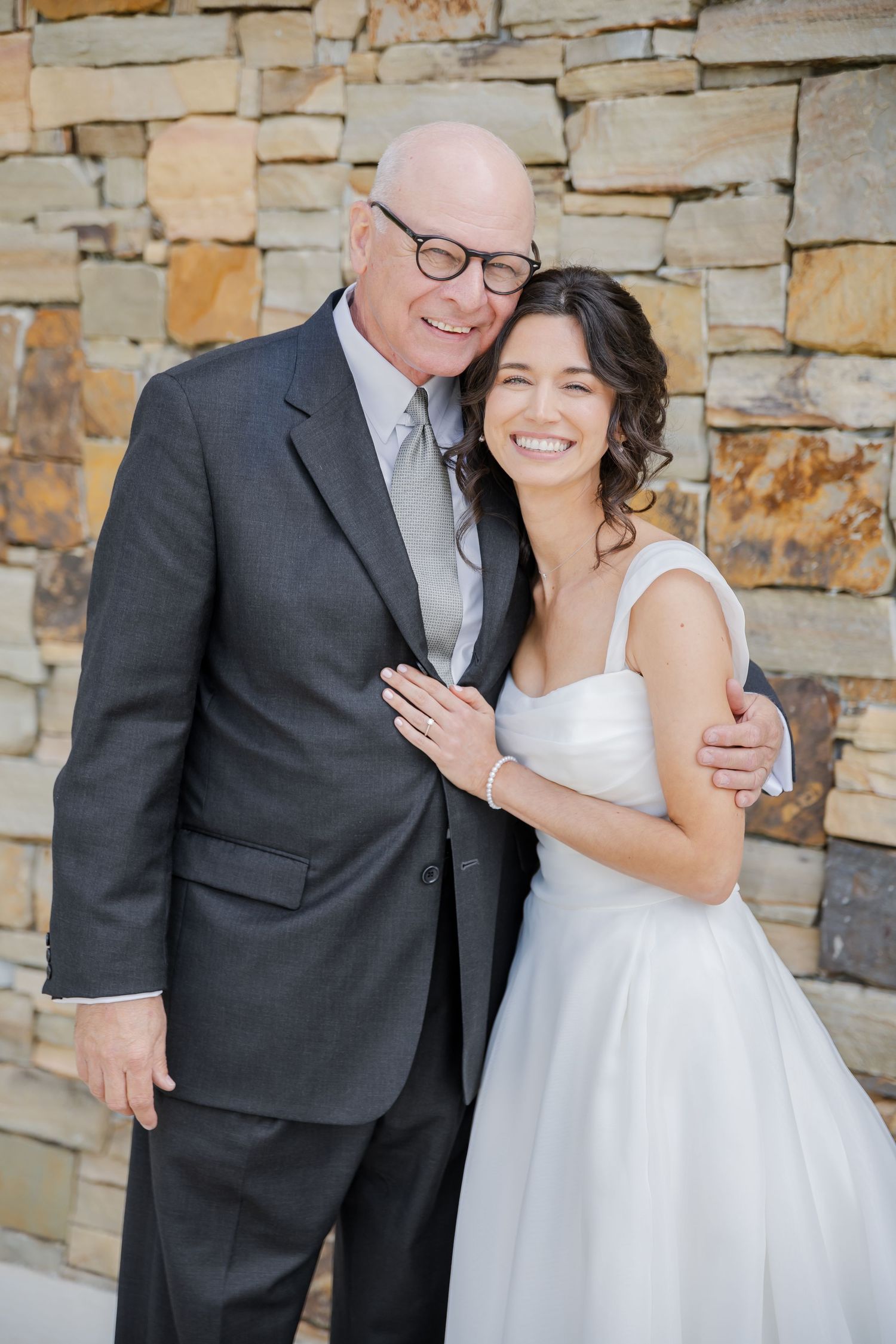 Sweet candid moments captured between a bride and groom sharing laughter against a stone wall backdrop.