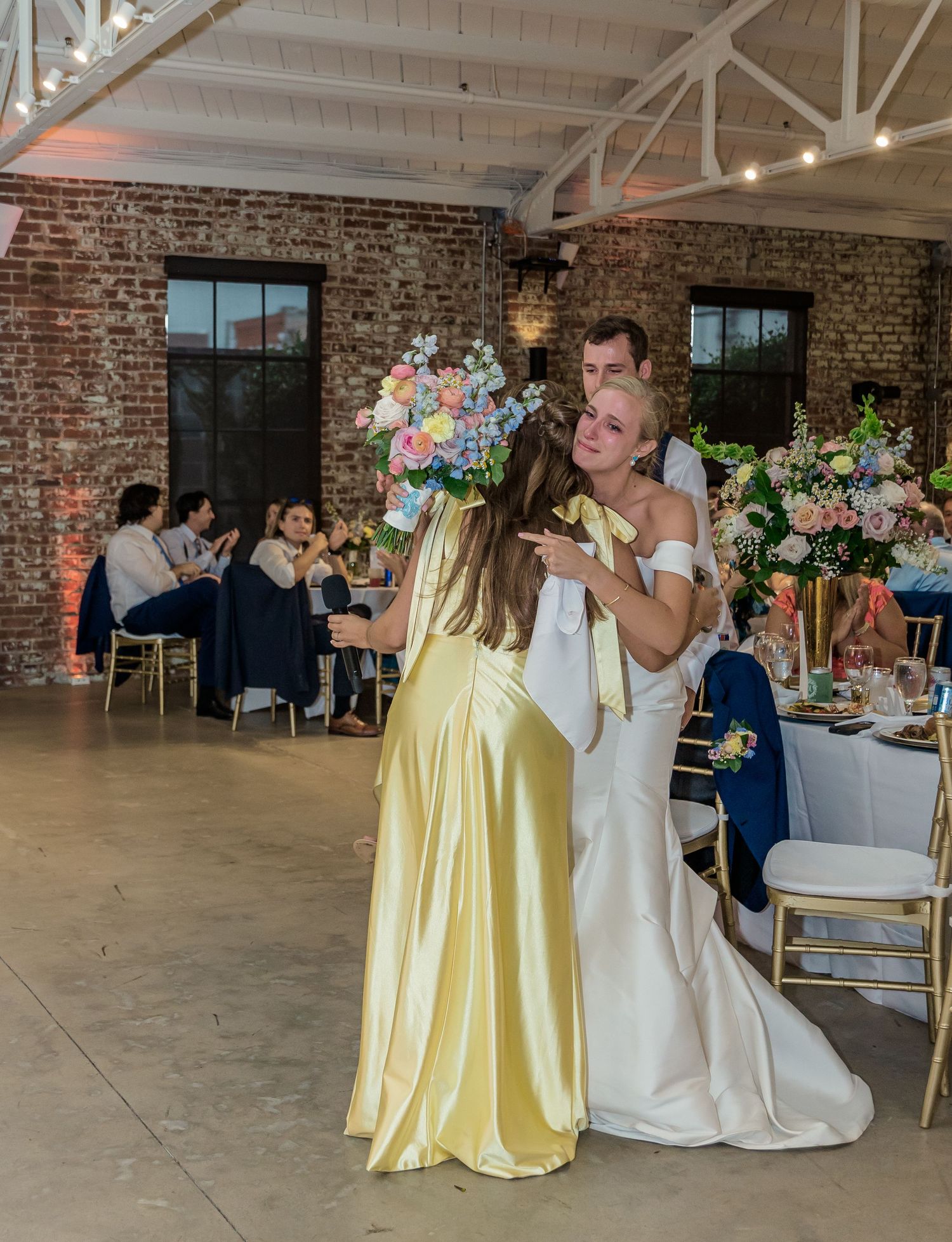 Wedding celebration in an industrial brick venue with yellow bridesmaid dresses and white decor.