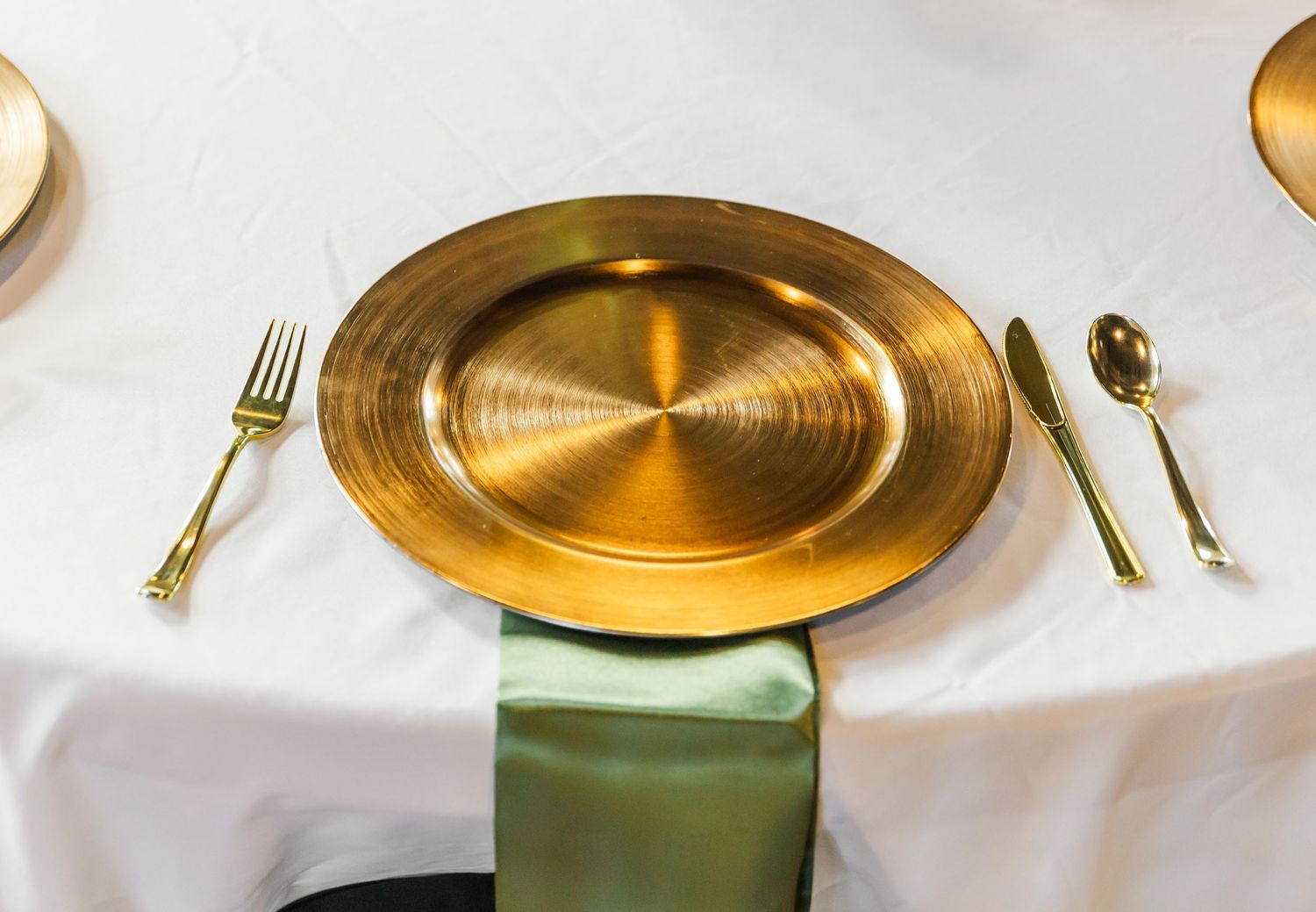 Gold charger plates and elegant place settings with sage green napkins on white tablecloth.