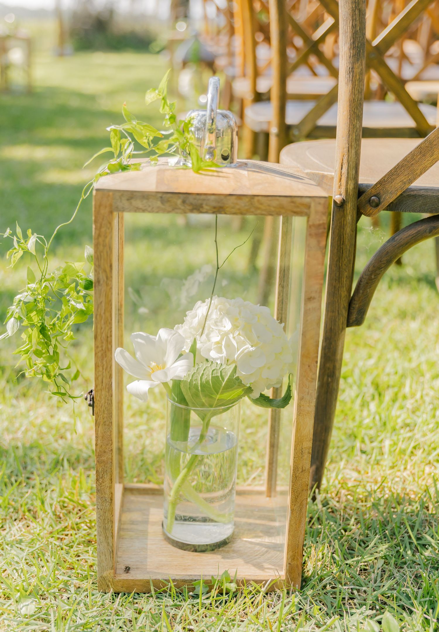 Rustic wooden lantern with delicate white flowers in a glass vase hanging as outdoor wedding decor.