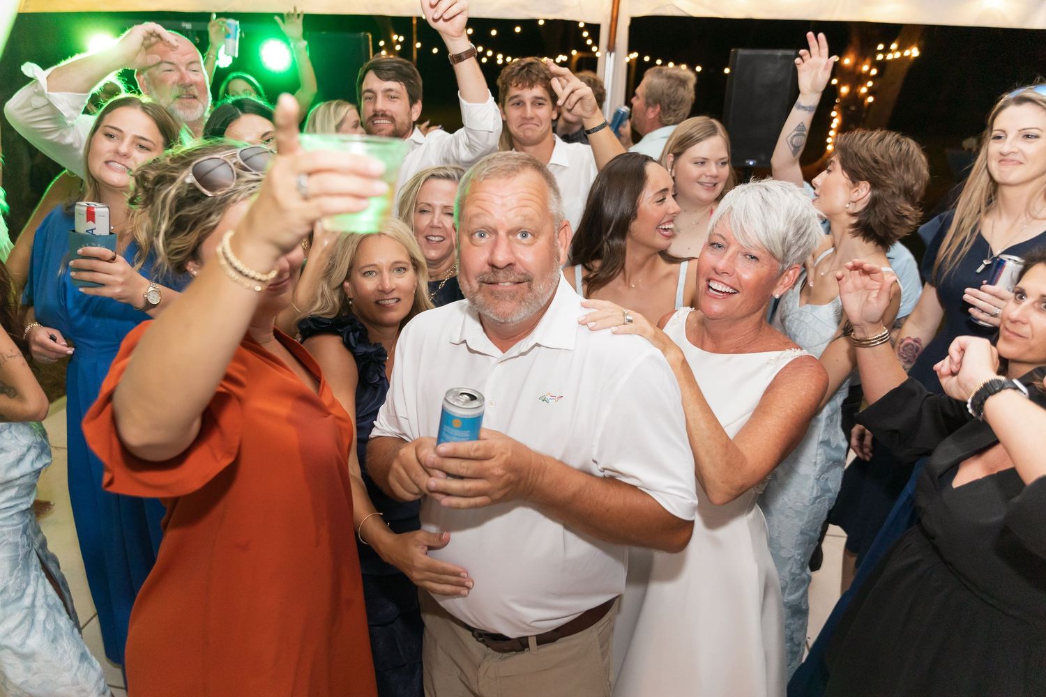 Wedding reception dance floor filled with guests enjoying the celebration under green lighting.