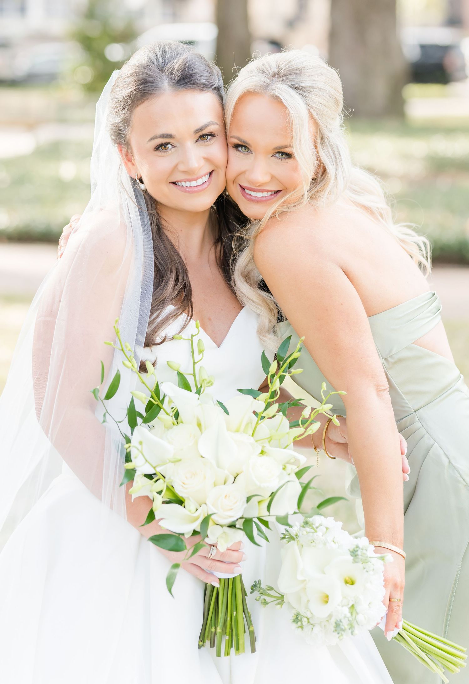 Wedding party members share joyful moments with white bouquets against natural backdrop.