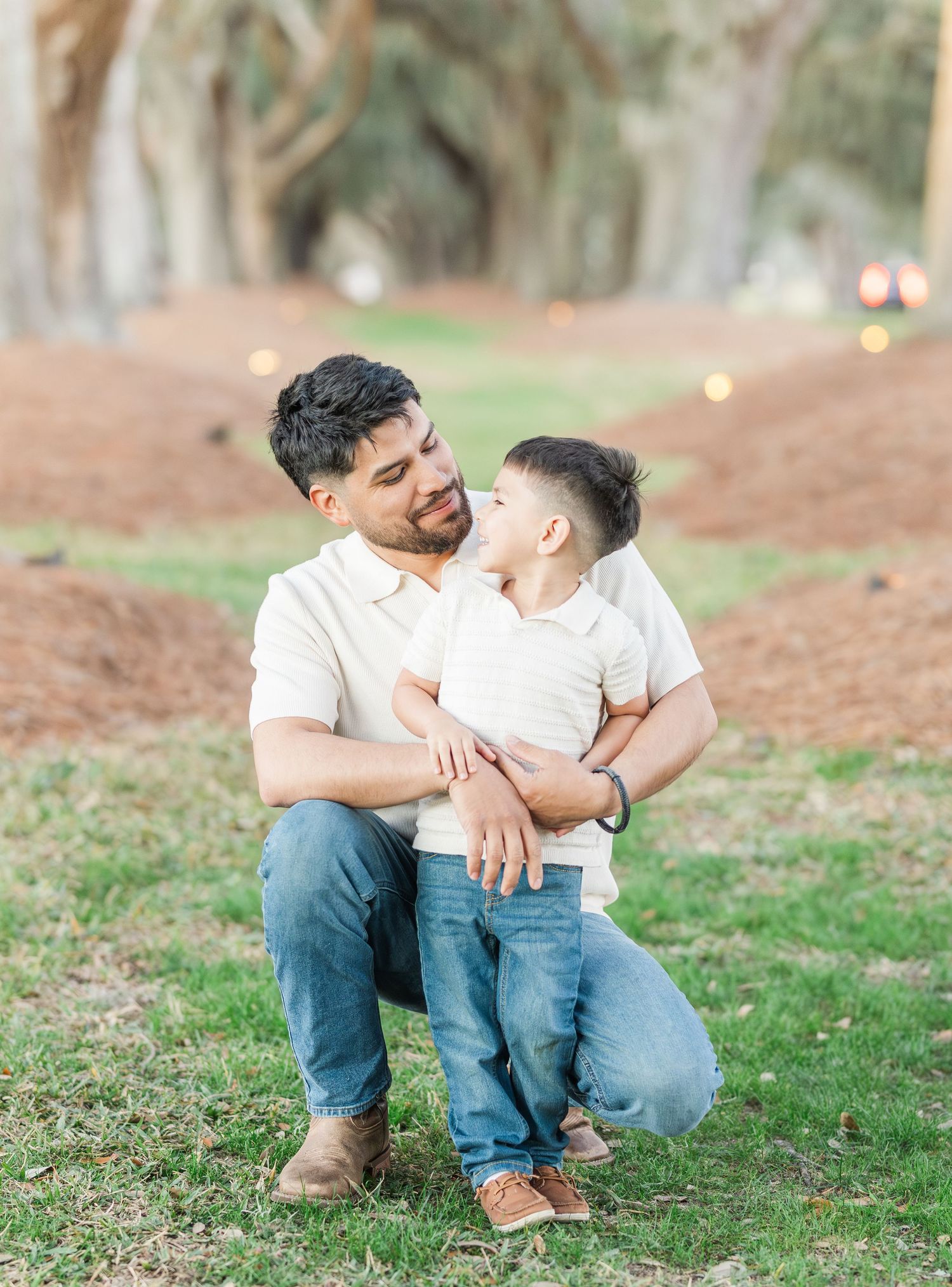 A touching moment between parent and child under tall trees in a park.