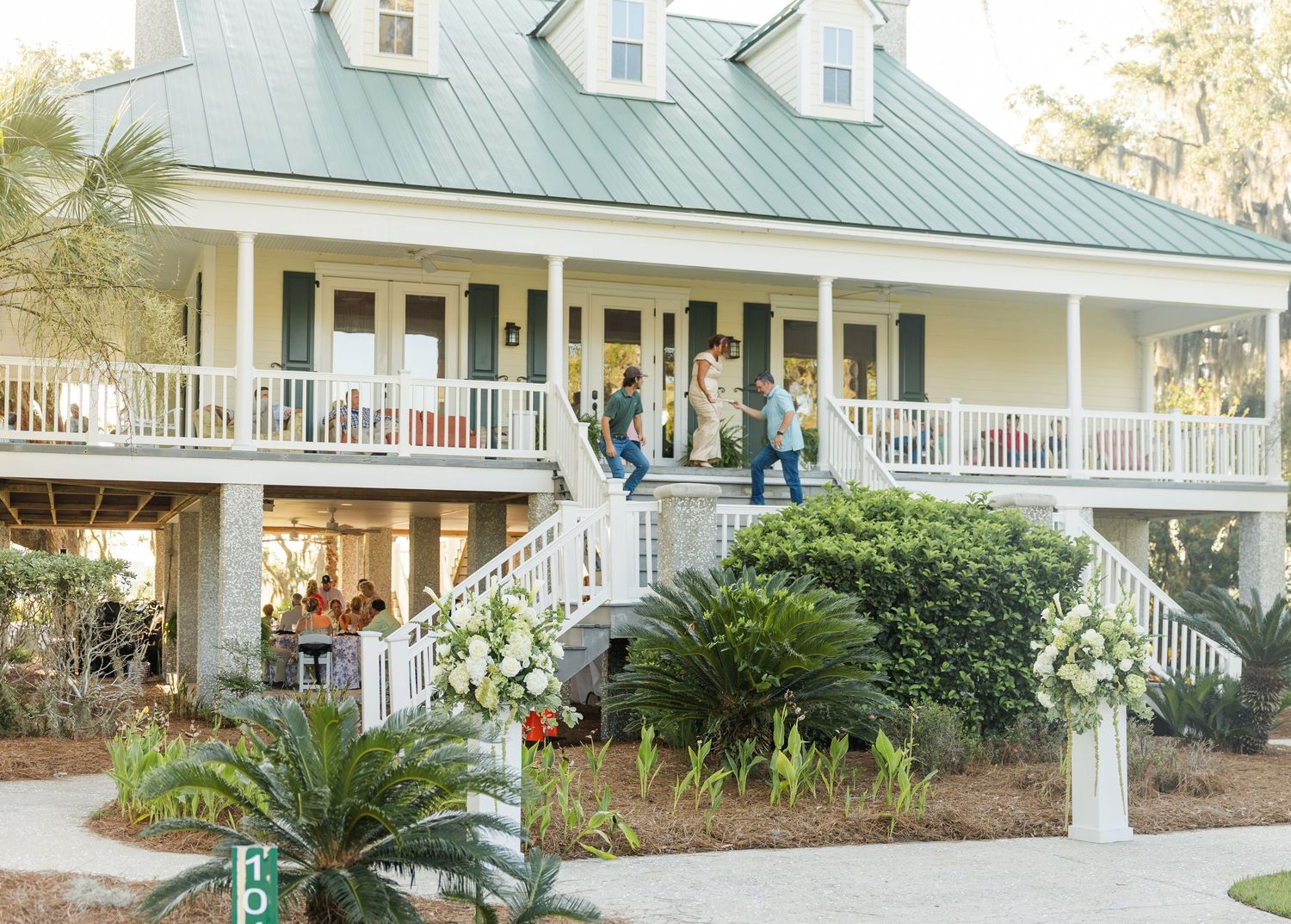 Elegant Southern plantation-style home with white railings, green metal roof, and floral arrangements for a wedding event.