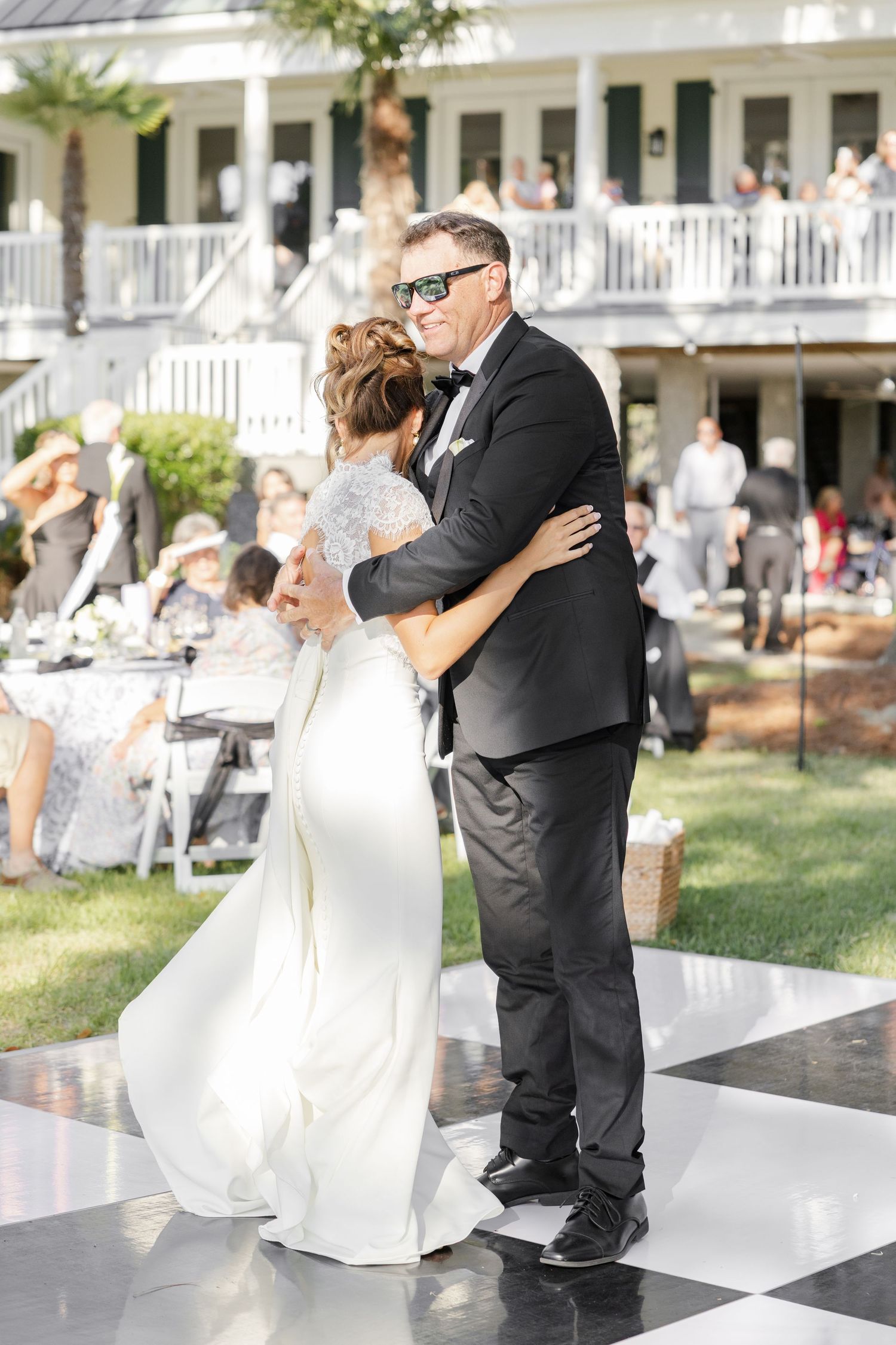 Bride and groom share first dance on checkered floor at outdoor wedding reception.