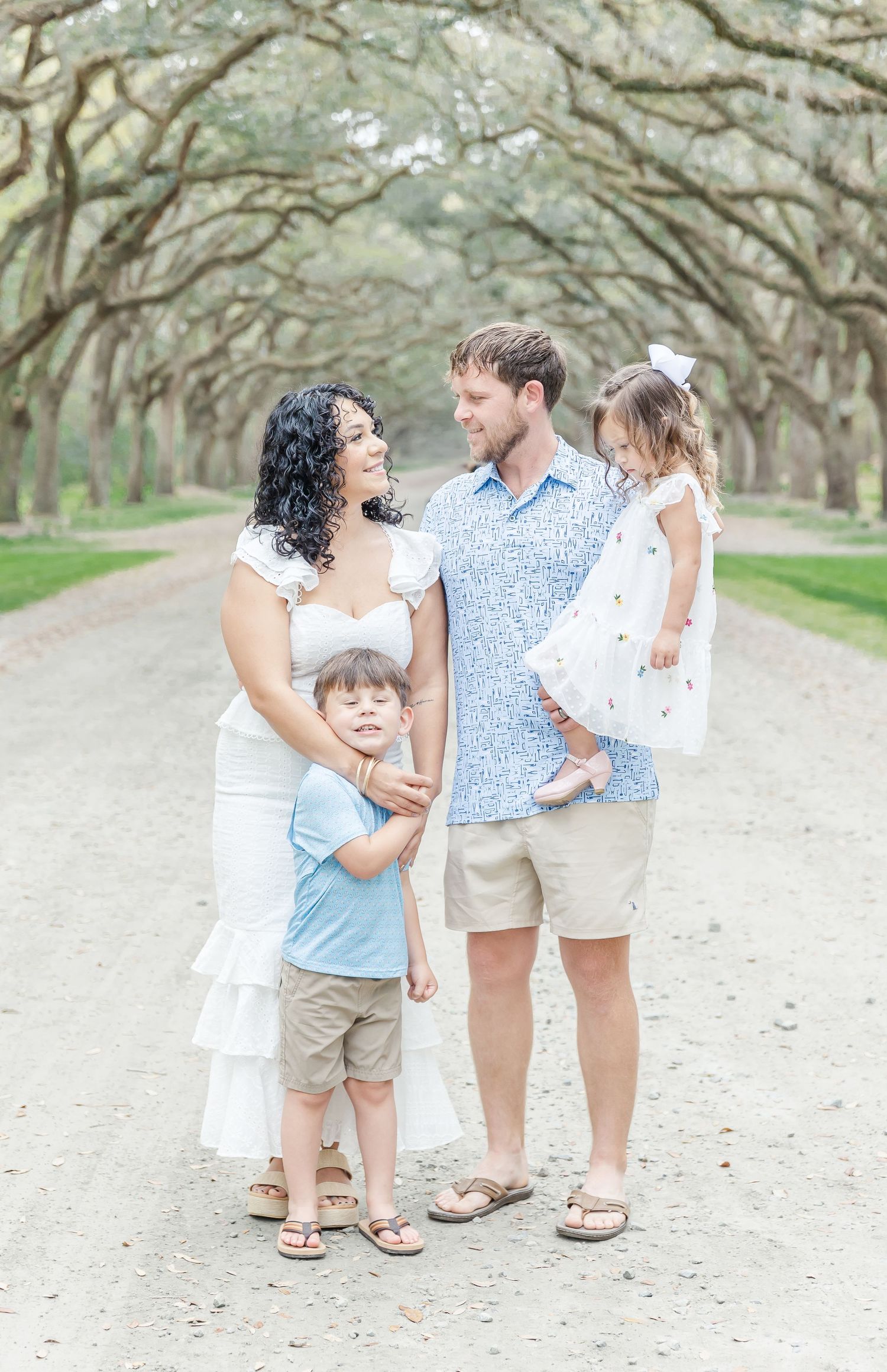 Sweet family moment captured under arching oak trees on scenic path.