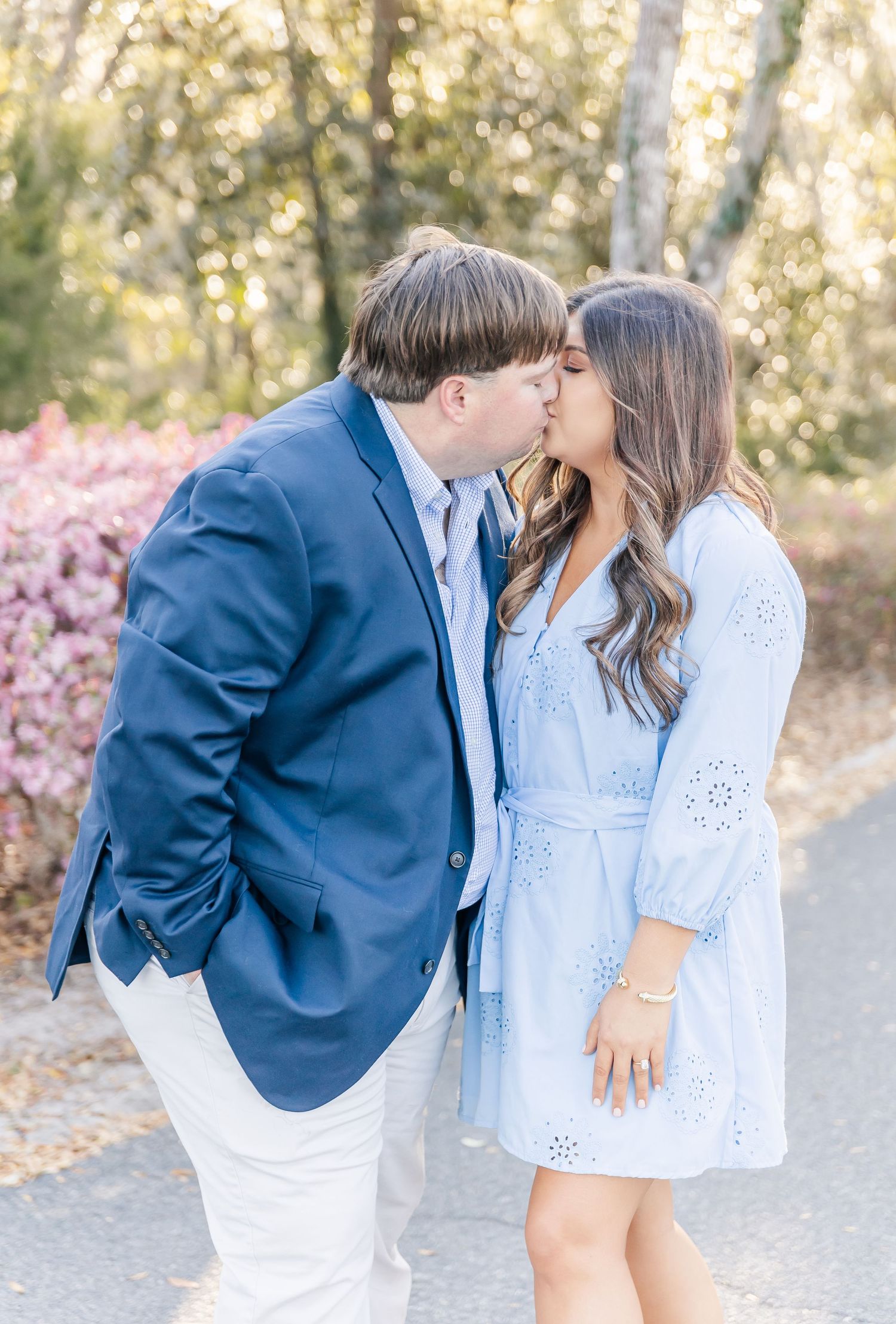 Couple sharing an intimate moment on a park path with pink flowers in background.