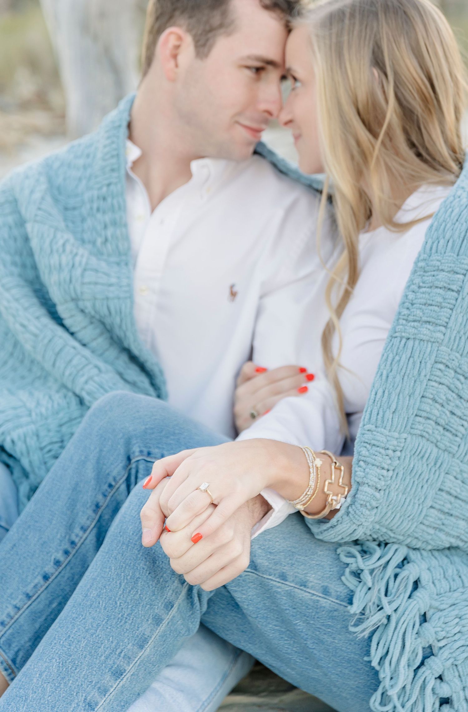Romantic couple sharing an intimate moment while wrapped in a cozy blue knit sweater on a beach.