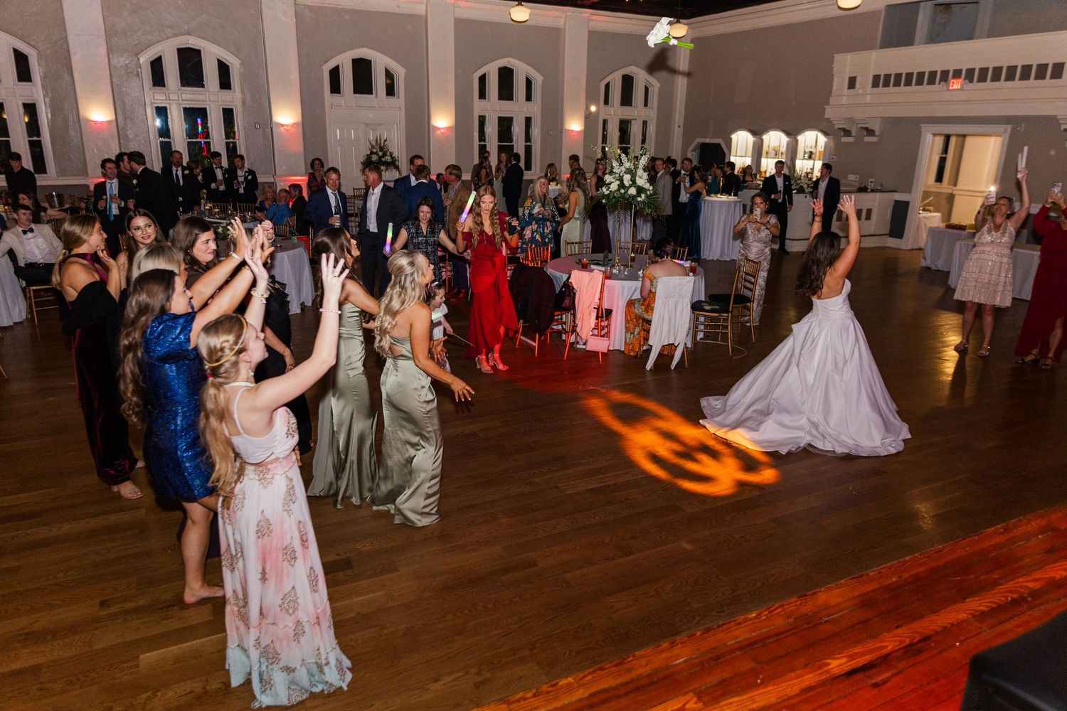 Bride tosses bouquet to excited guests on the dance floor at a wedding reception.