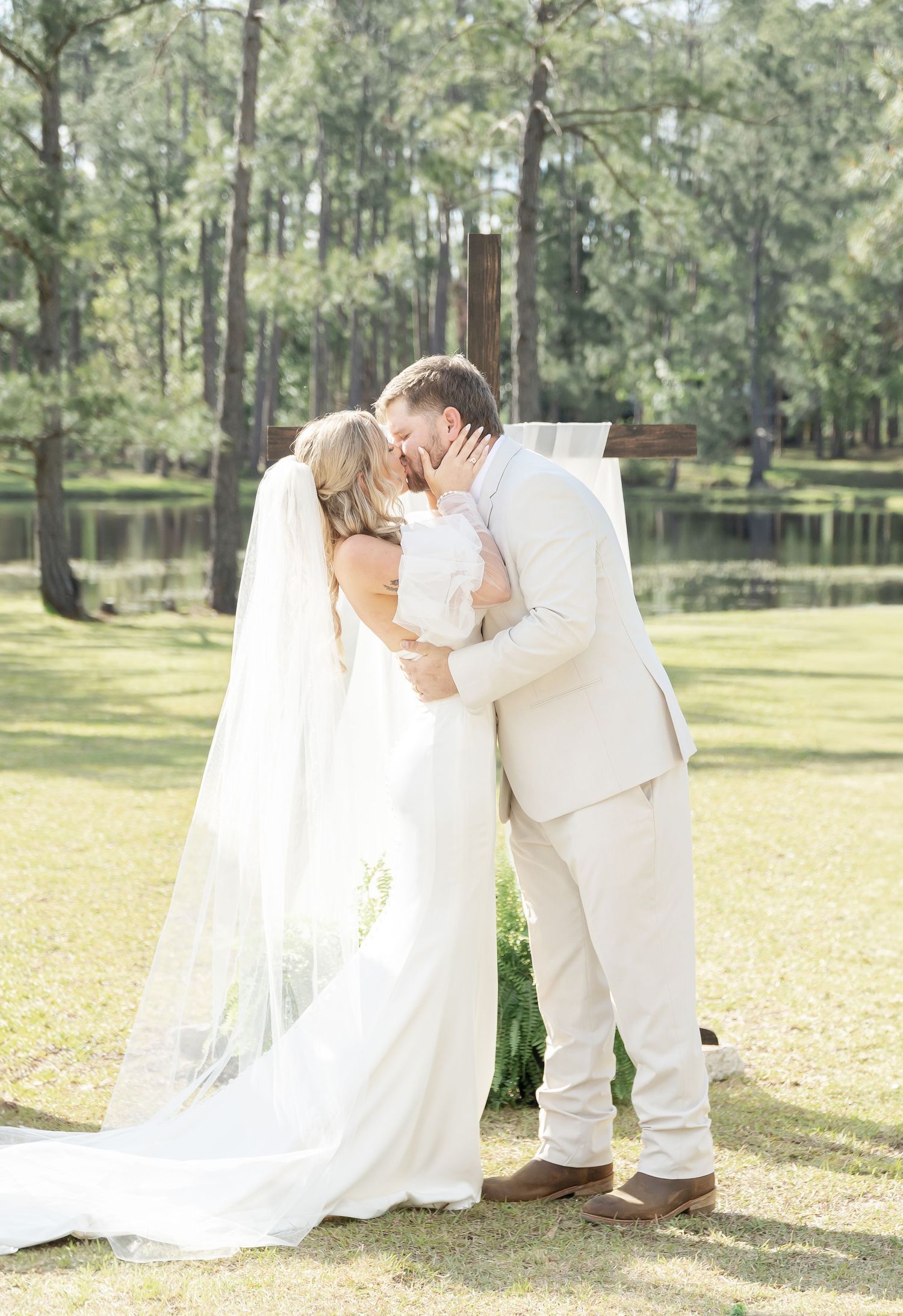Intimate wedding moment captured in soft sunlight with pine trees and lake in the background.
