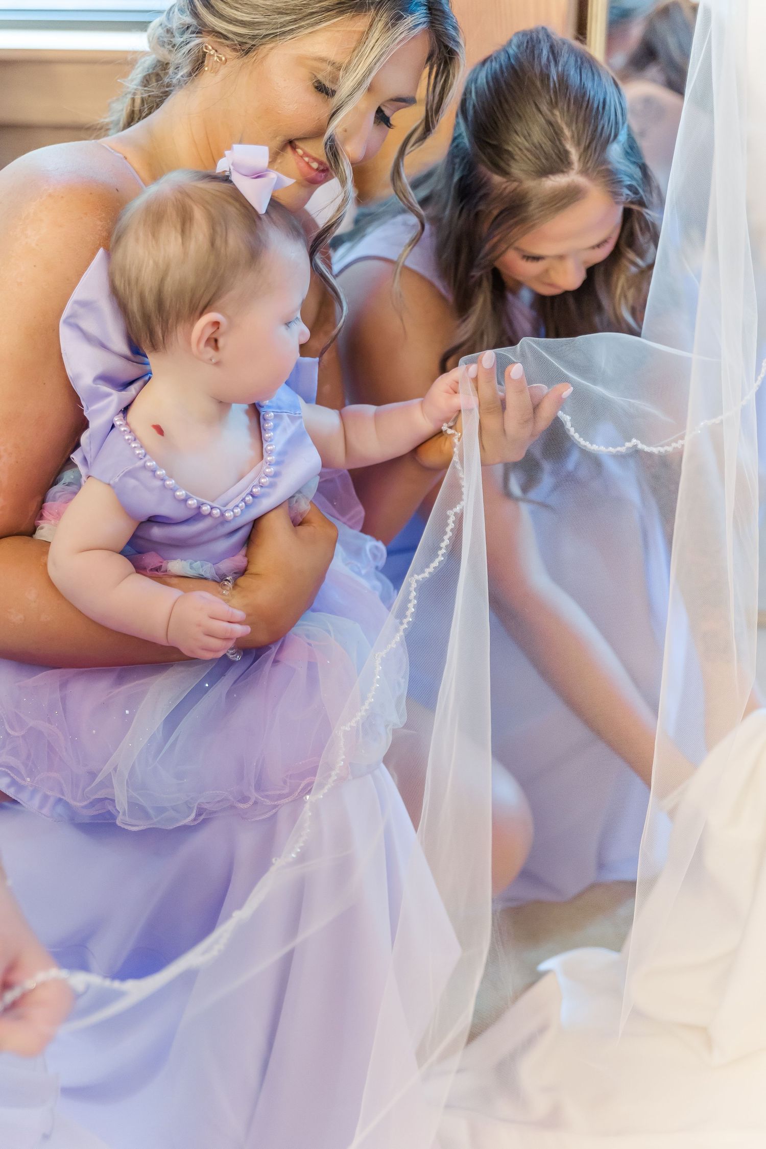 Sweet moment as bridesmaids in purple dresses interact with a baby during wedding preparations.