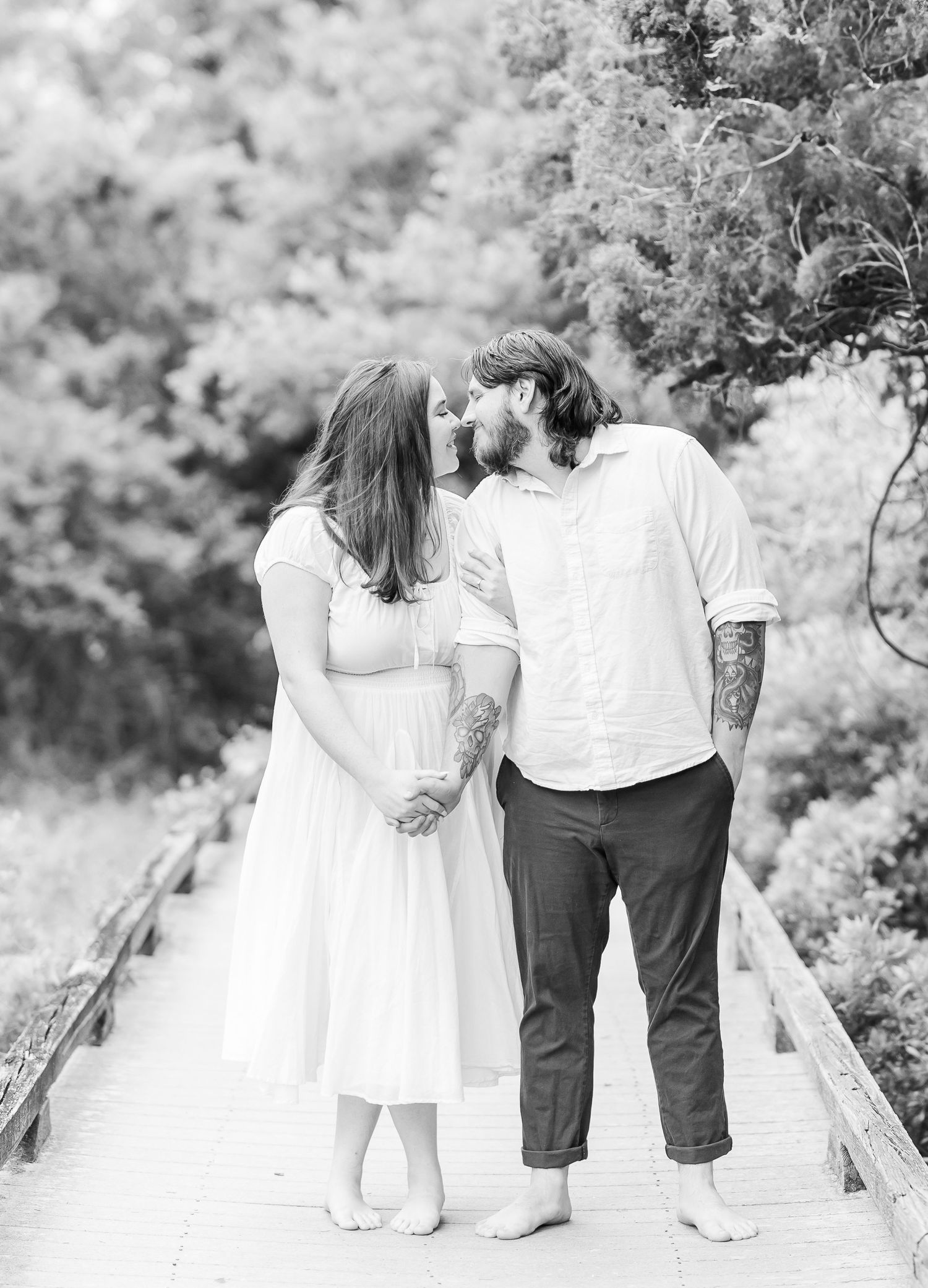 Black and white portrait of couple sharing intimate moment on boardwalk.