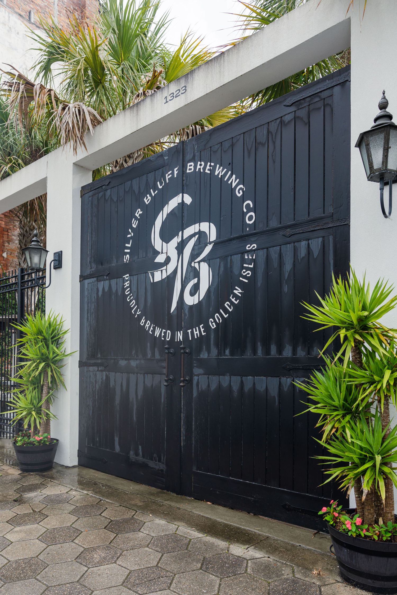 Black wooden gates with Silver Bluff Brewing Co. logo, flanked by tropical plants and lanterns.