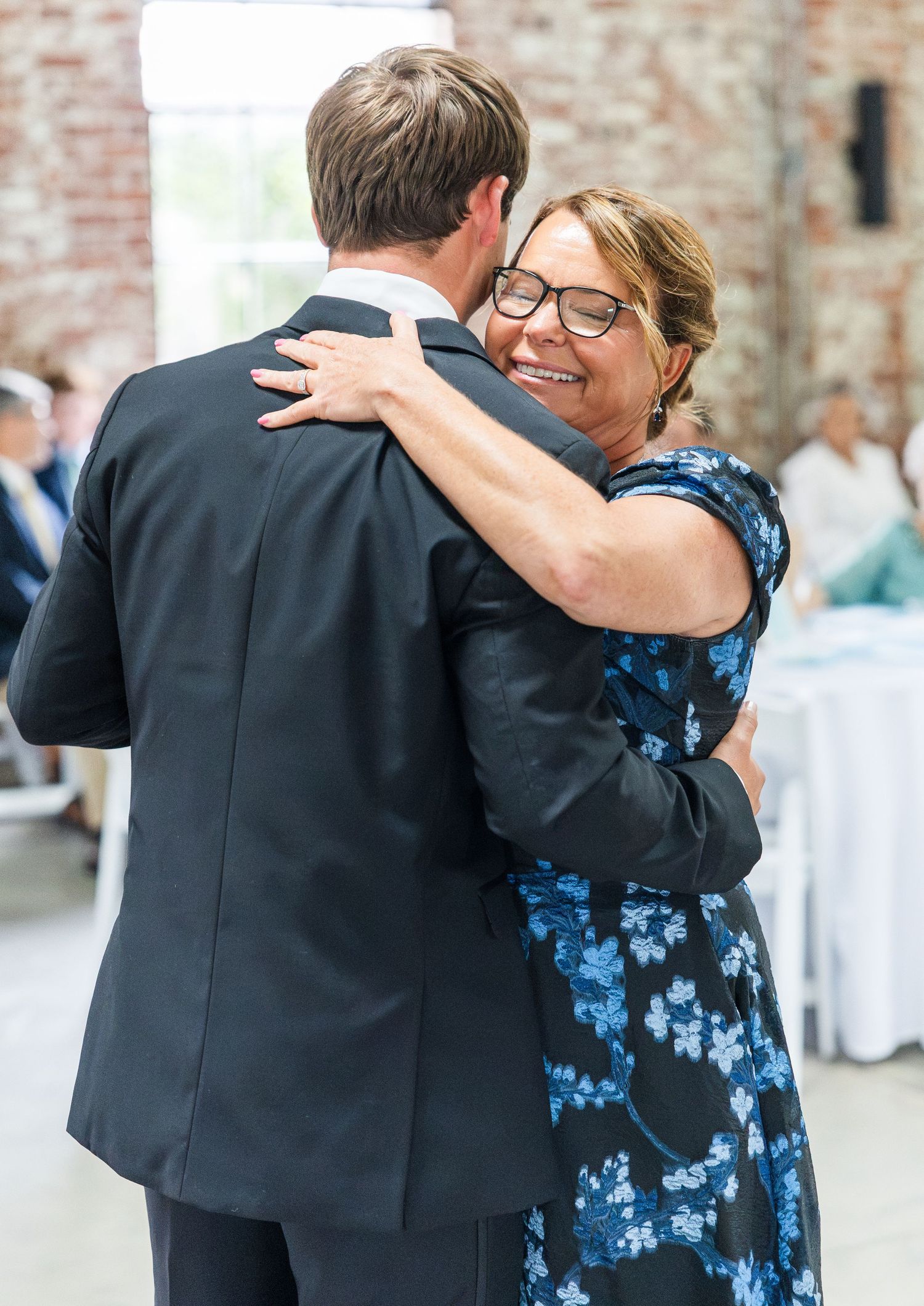 Woman in blue floral dress smiling while sharing a dance with groom at wedding reception.