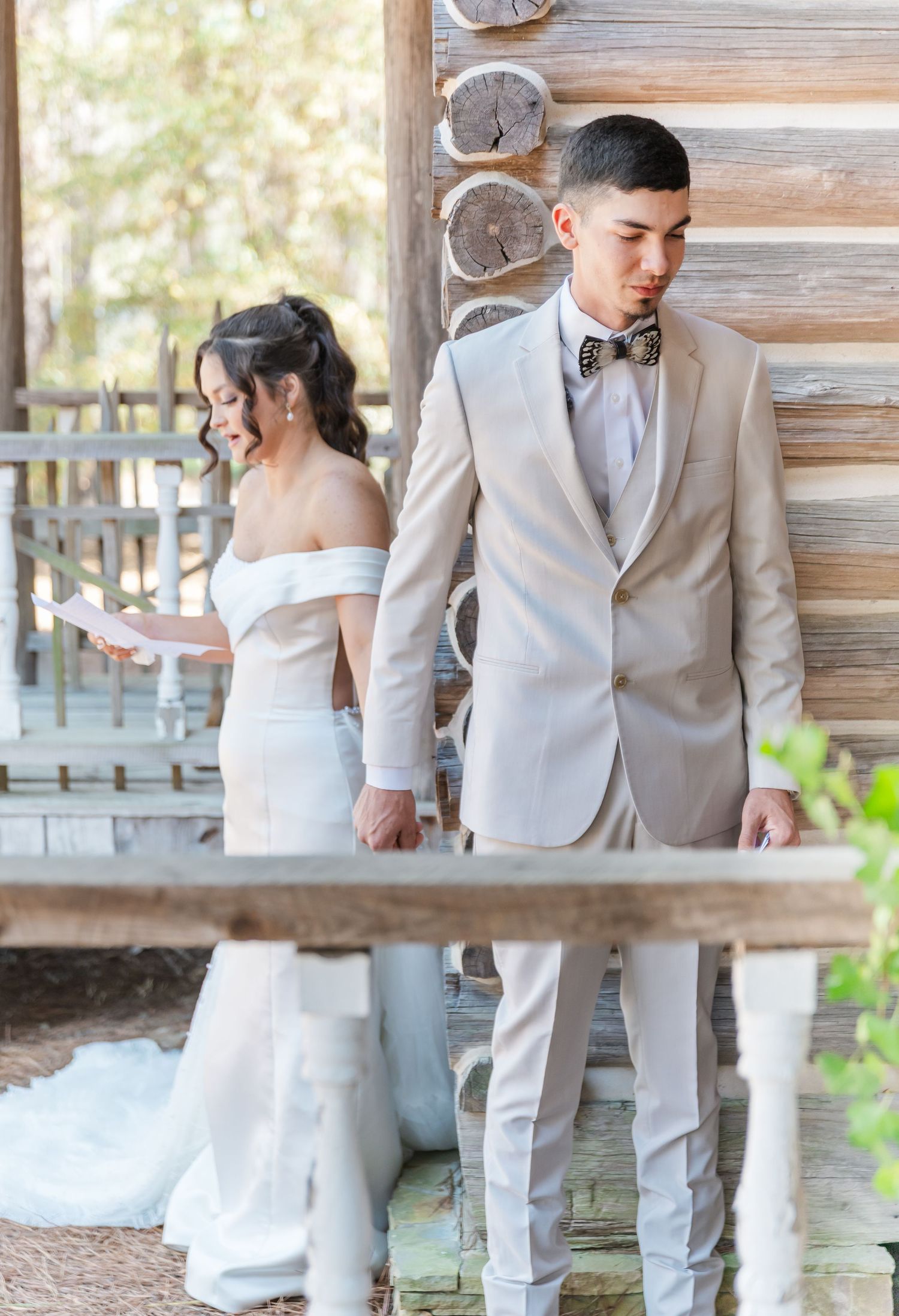 Bride and groom share a private first look moment at rustic log cabin venue, reading vows back to back.