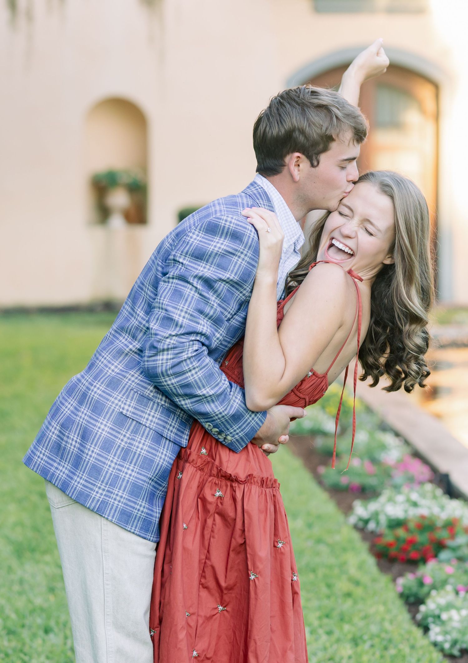 A playful romantic moment captured in a garden with Spanish-style architecture.