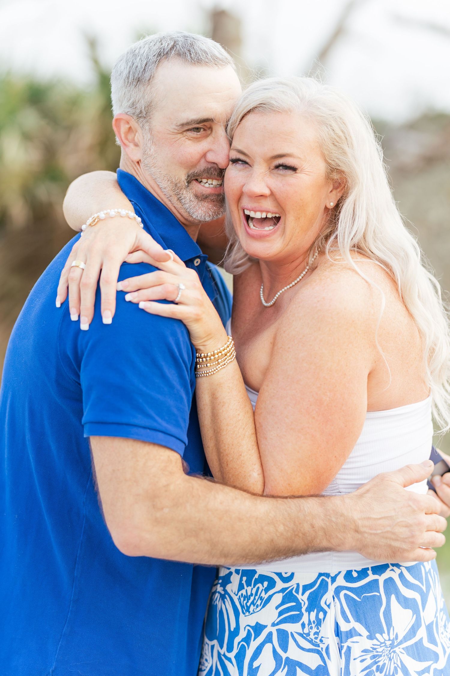 Joyful couple embraces and laughs while wearing blue and white outfits during outdoor photo session.