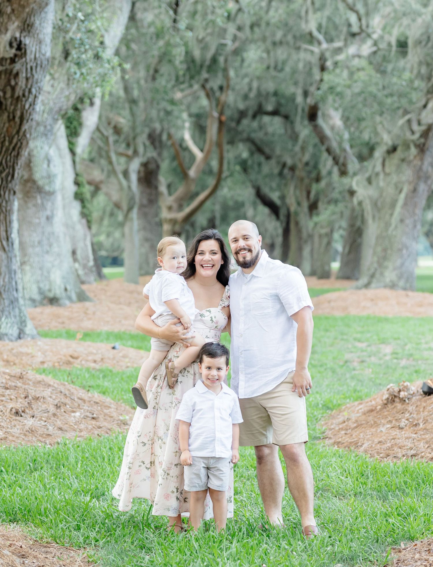 A family poses together on a grass path lined with mossy oak trees creating a dreamy outdoor setting.