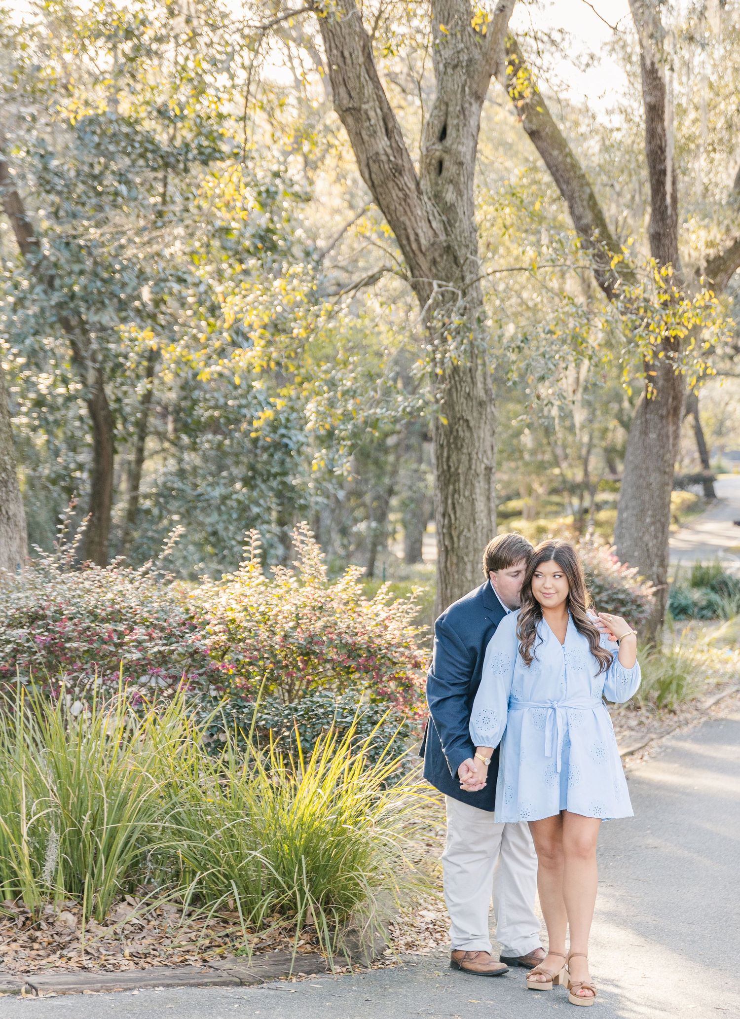 A couple poses together on a garden path surrounded by autumn trees and ornamental grasses.