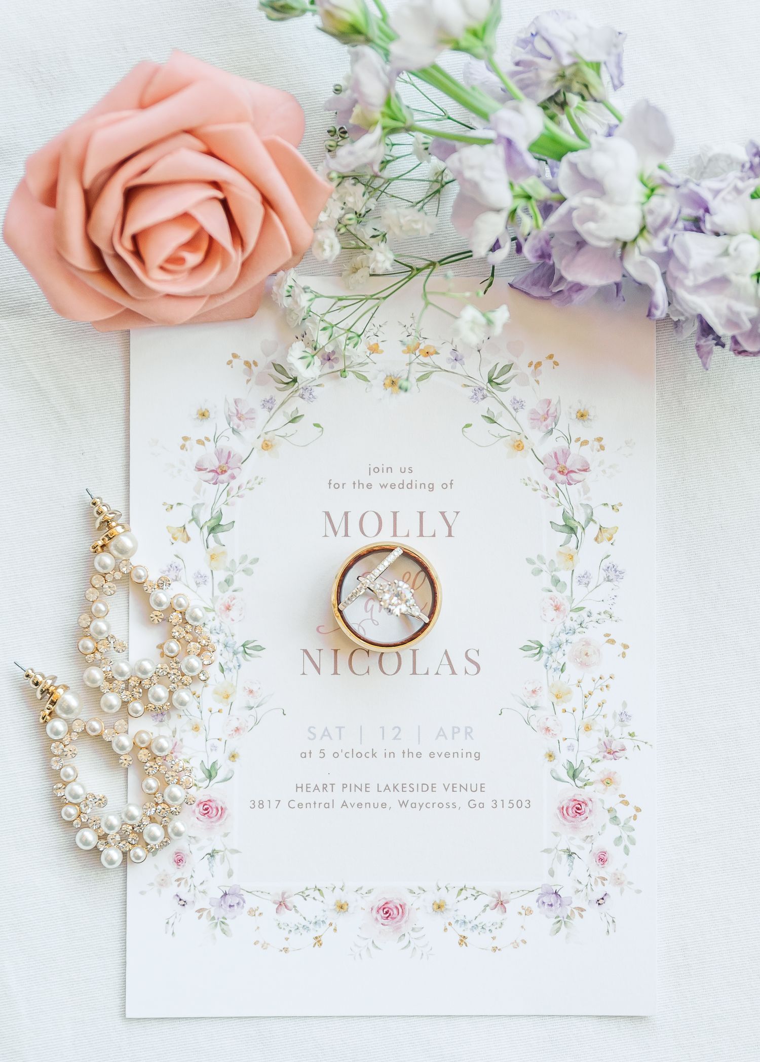 Elegant wedding invitation with peach roses, pearl jewelry, and delicate floral details arranged on white background.