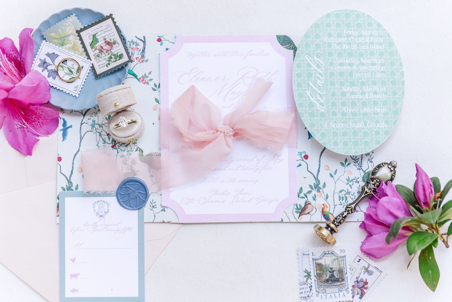 A pastel flat lay arrangement with pink flowers, blue decorative items, and delicate bow against a white background.