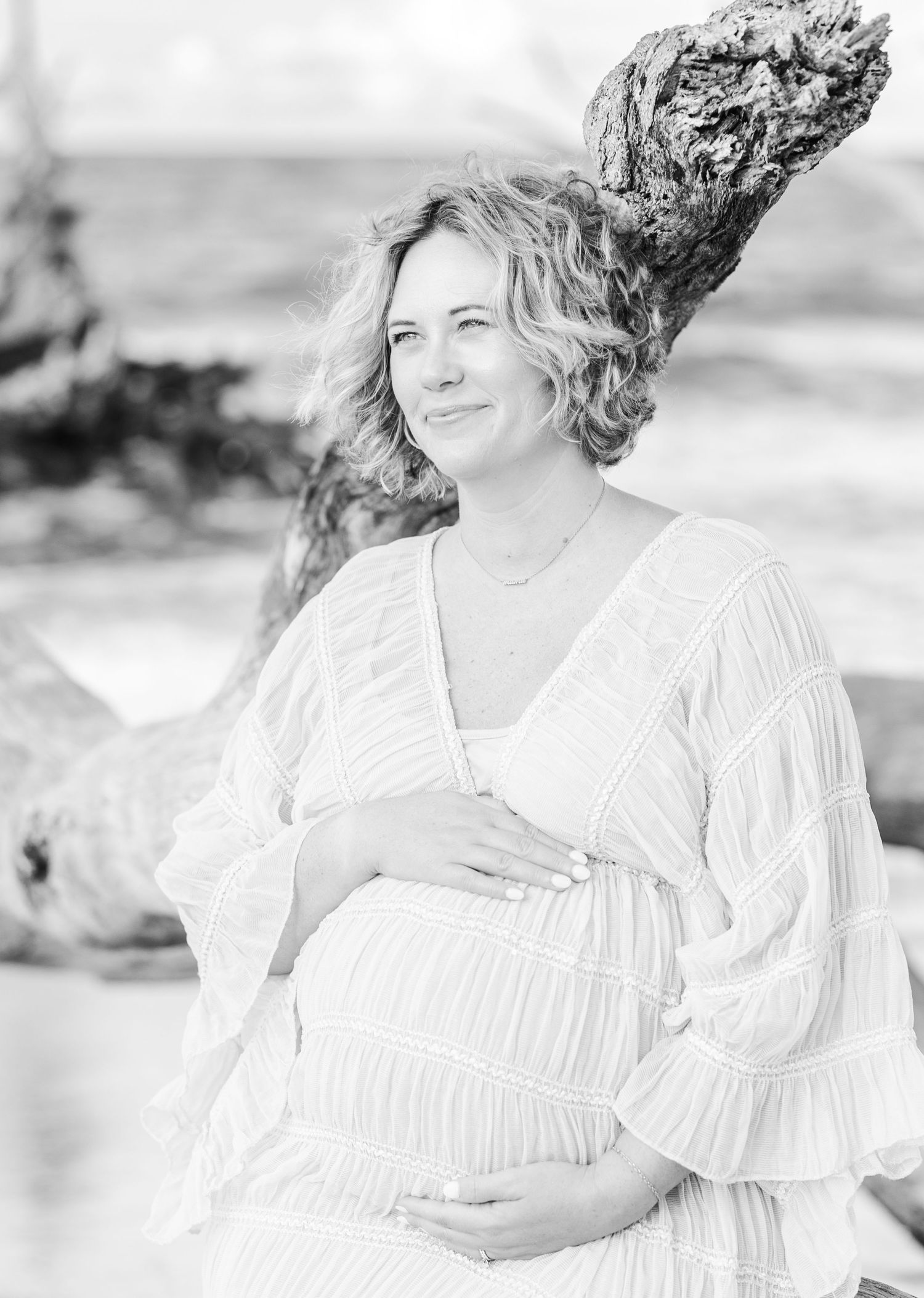 A peaceful maternity portrait in black and white against driftwood on the beach.