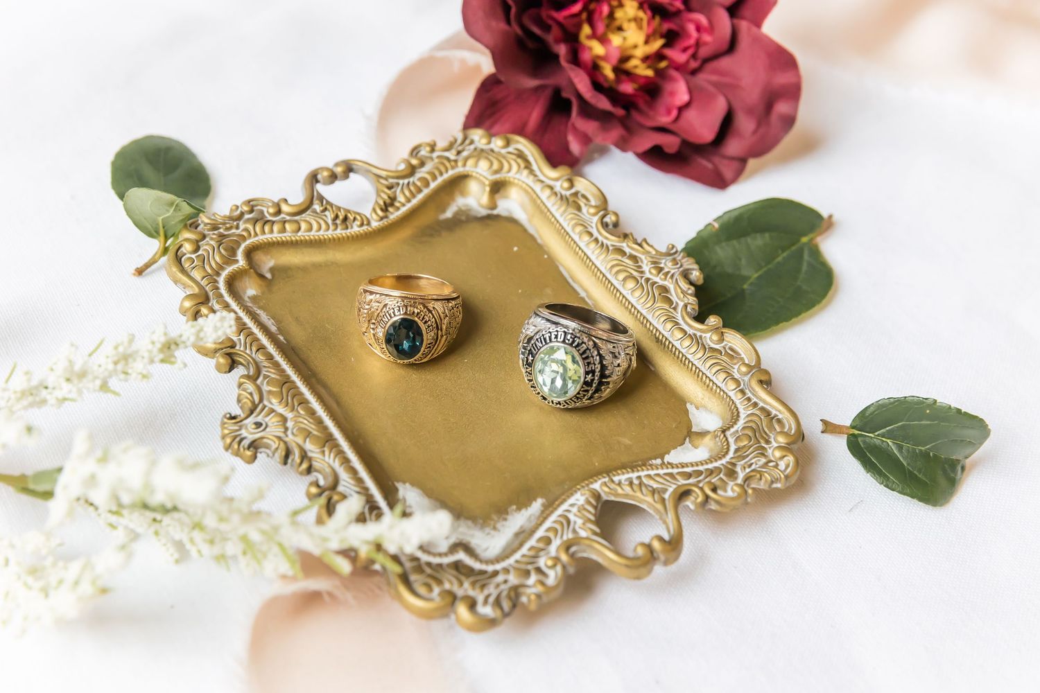Elegant gold jewelry pieces with floral designs and red blooms arranged on a light background.