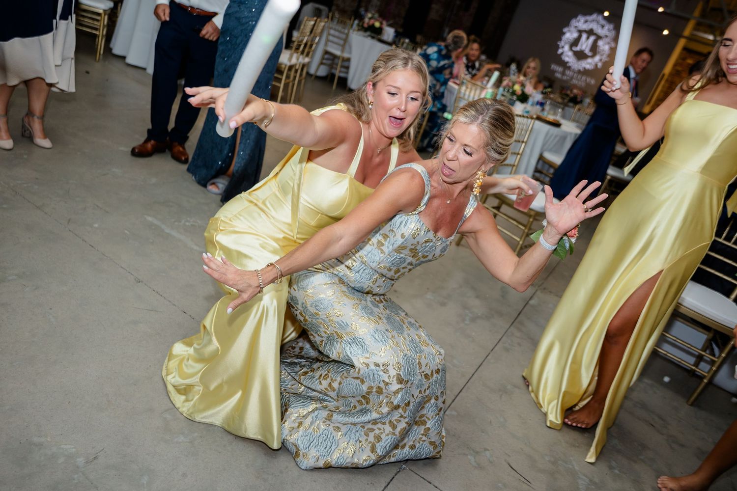 Party guests in yellow and silver dresses strike playful dance poses at a celebration event.