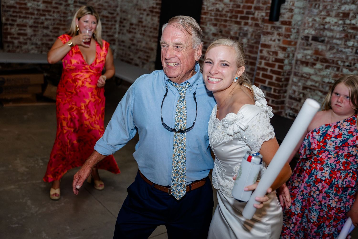 Guests dance with glowing foam sticks at a brick-walled reception venue.