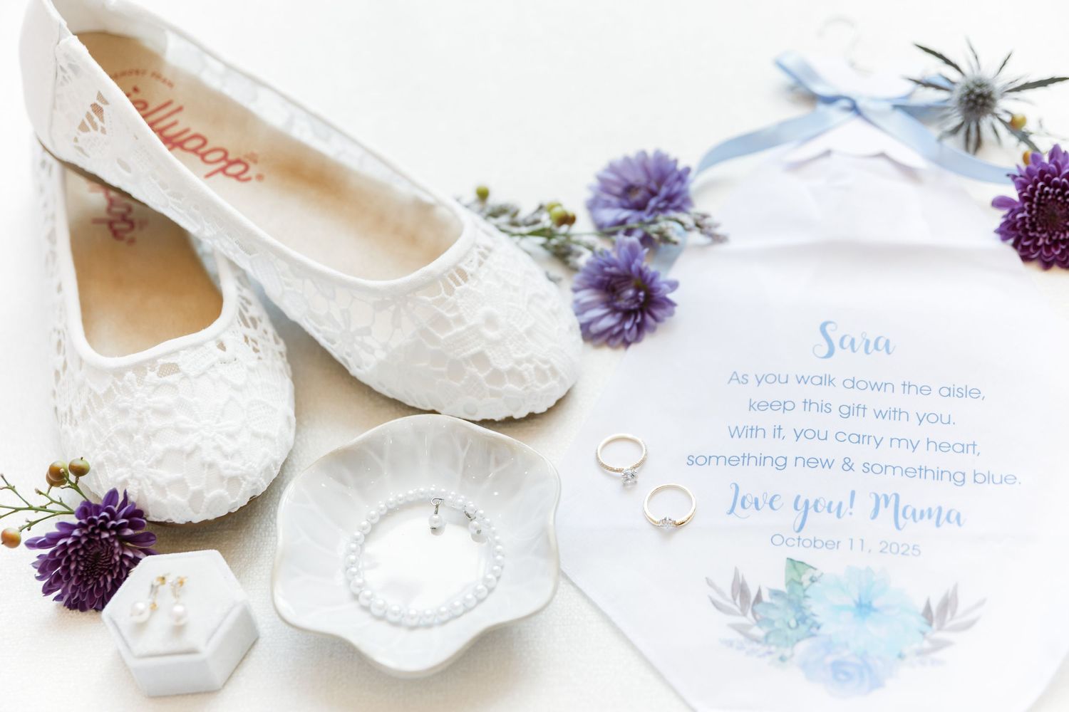 White lace ballet flats arranged with purple flowers and wedding stationery on a light background.