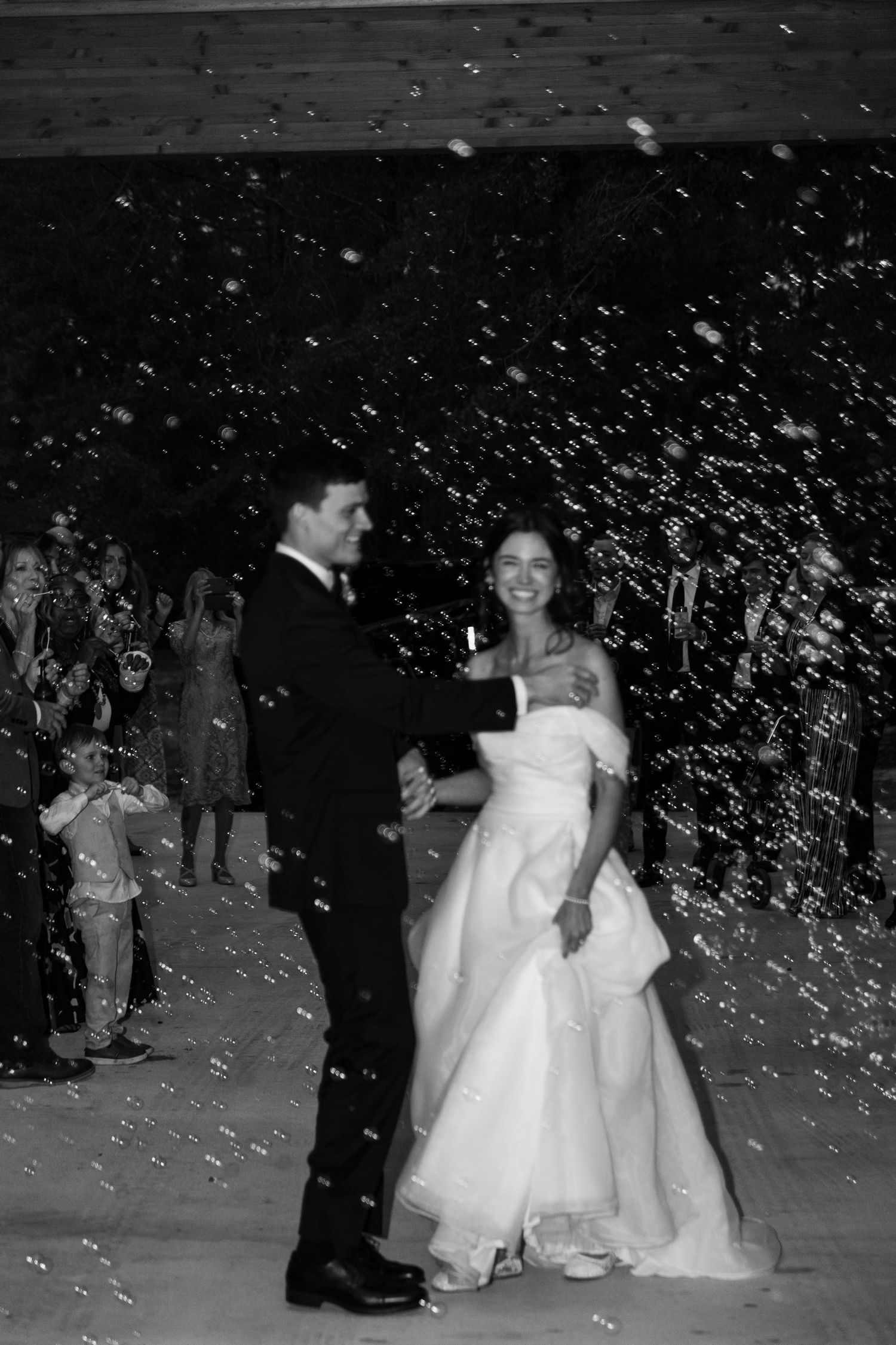 A black and white photo captures a newlywed couple amid a shower of confetti at their wedding celebration.
