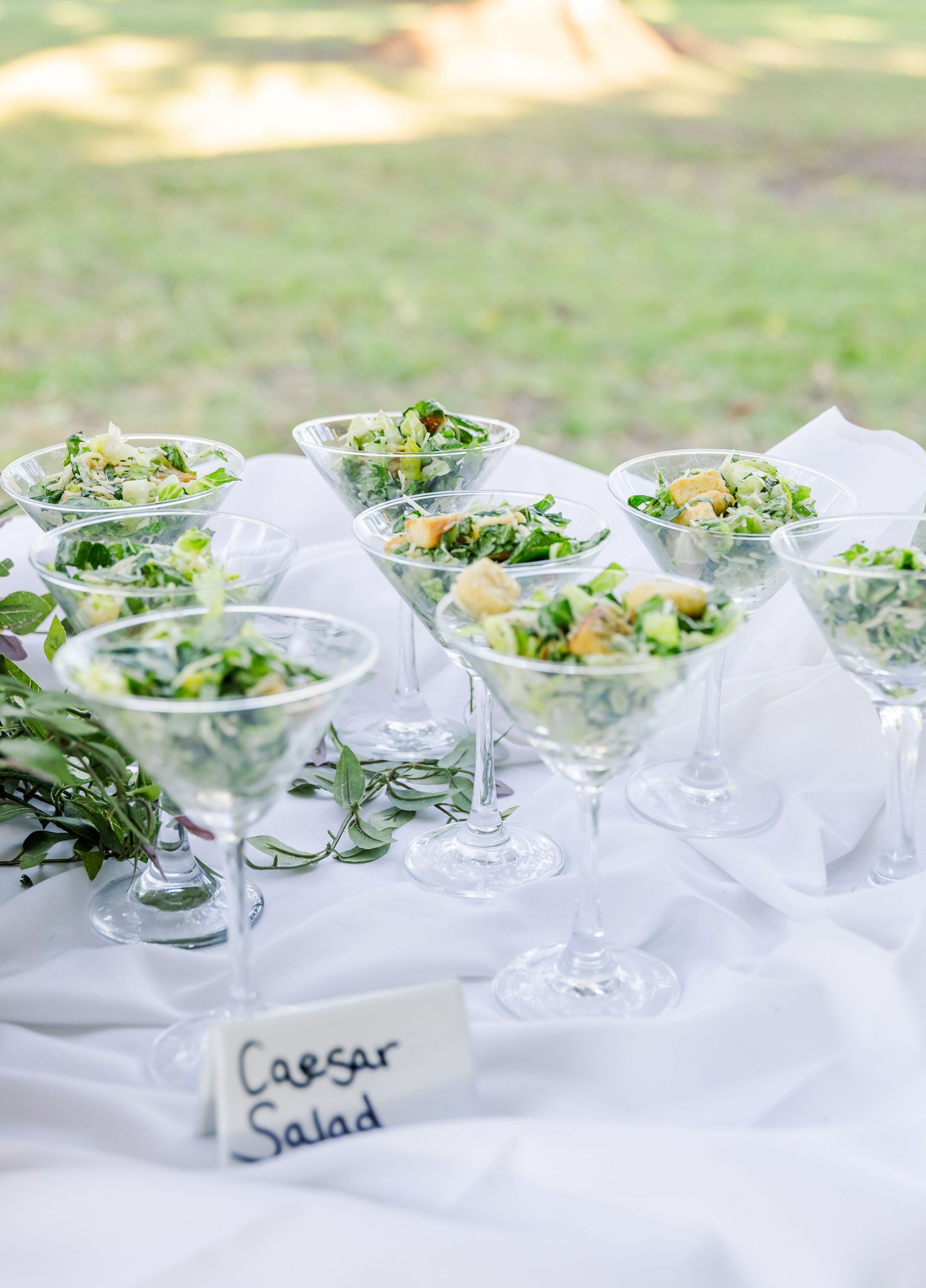 Individual Caesar salads served in martini glasses on an elegant white tablecloth.