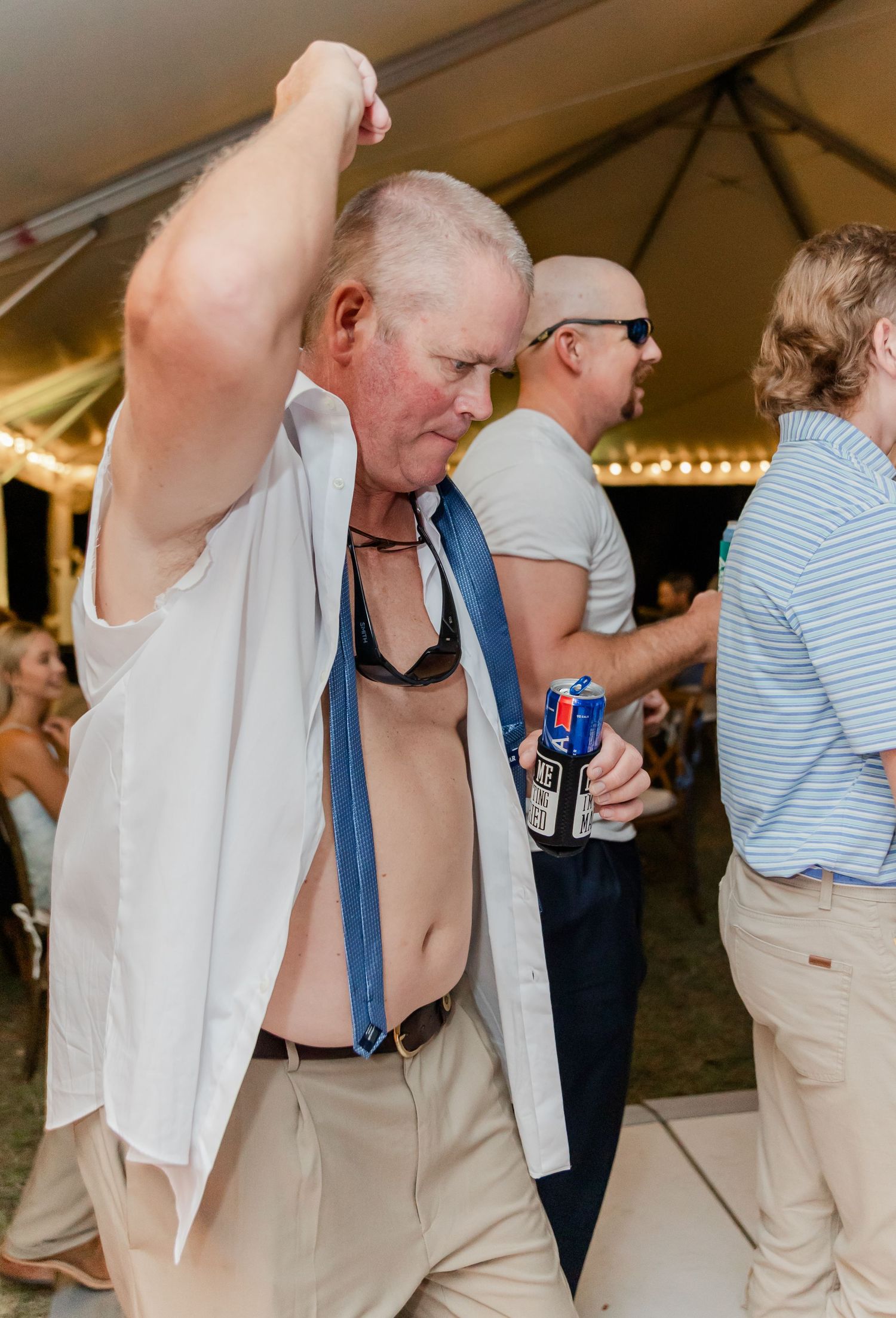 Party guests in casual attire dance and socialize under a white tent during an outdoor event.