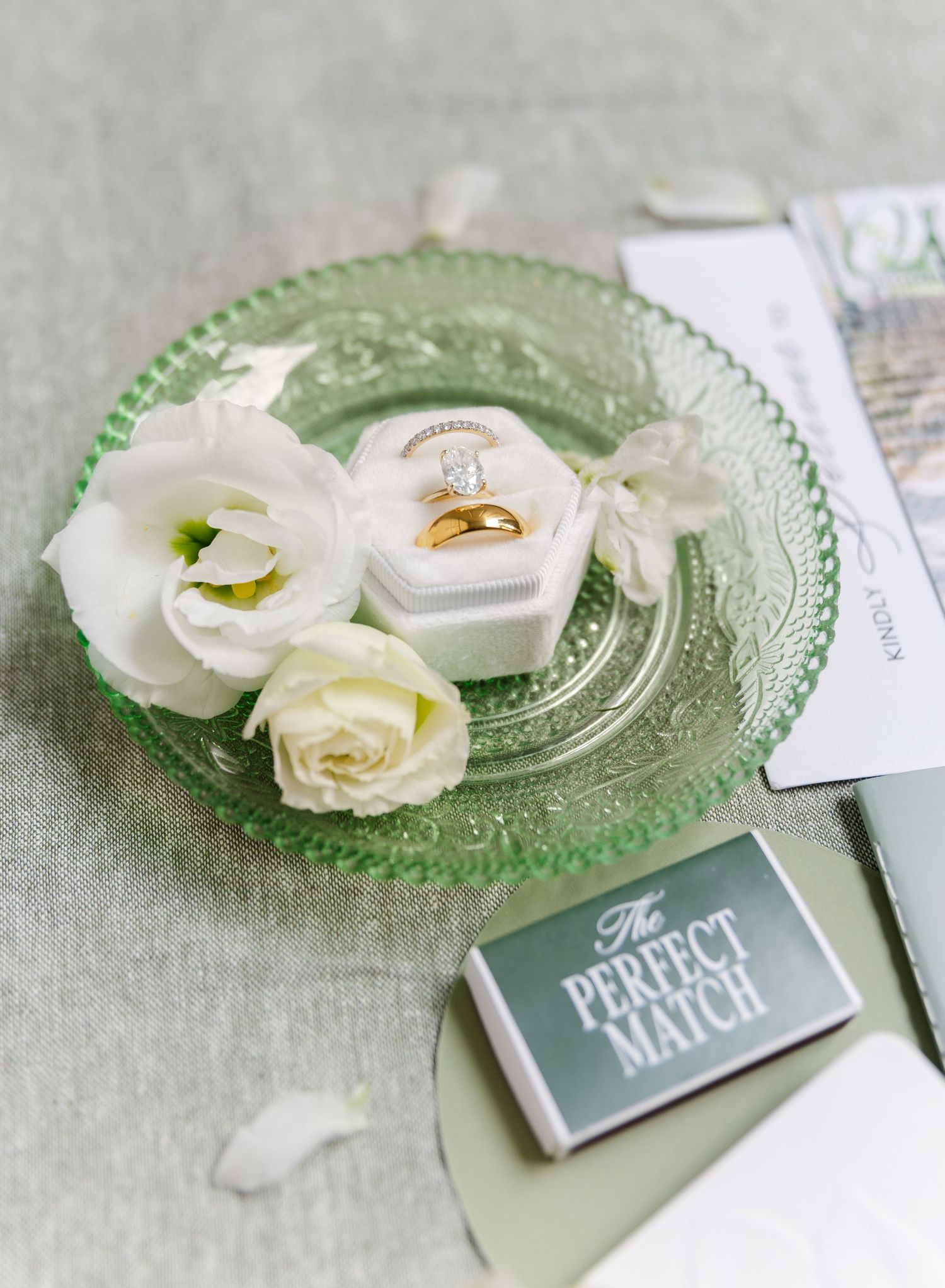 White roses and wedding rings displayed on a decorative green glass plate with matching cards.
