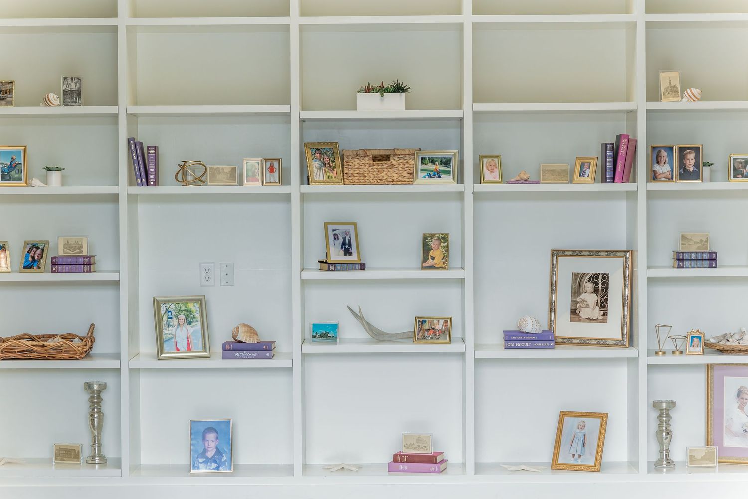 White built-in shelving unit displaying framed photos, books, and decorative objects against a light wall.