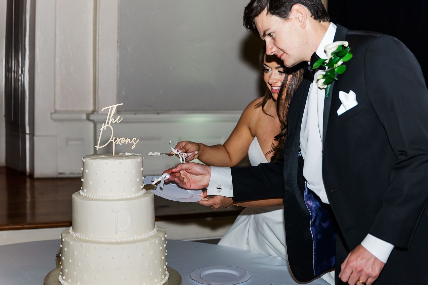 Wedding cake cutting moment with couple in formal attire at reception.