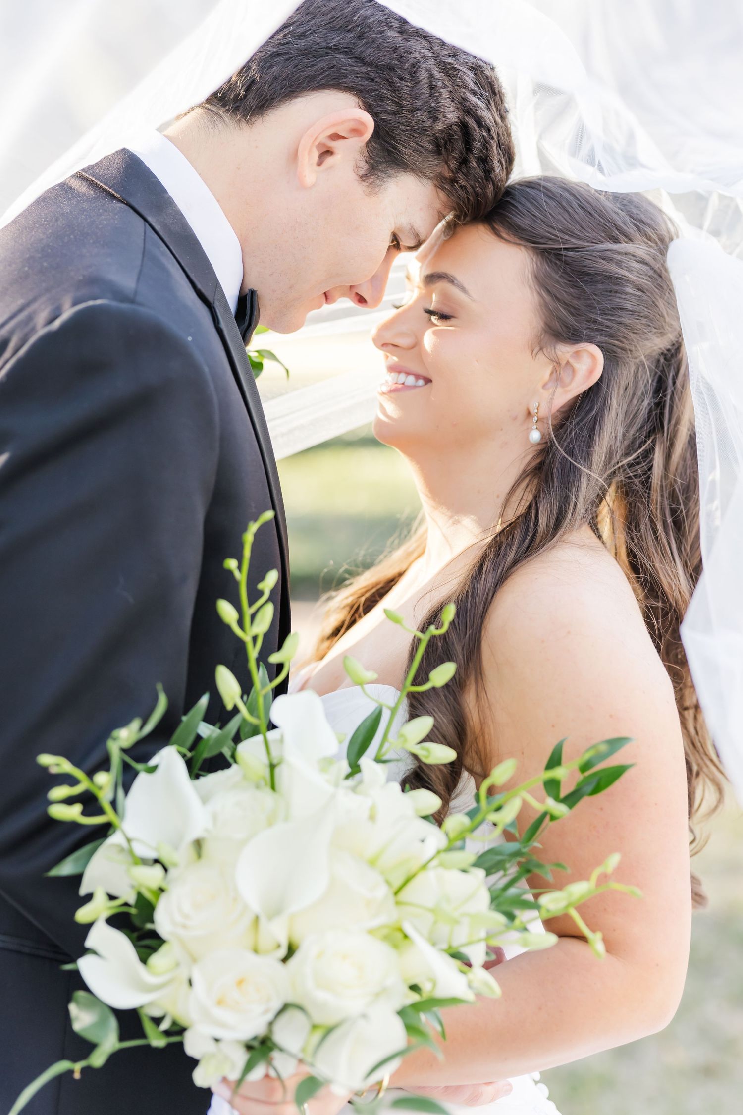 A romantic wedding couple shares intimate moments outdoors with a bouquet of white lilies and greenery.