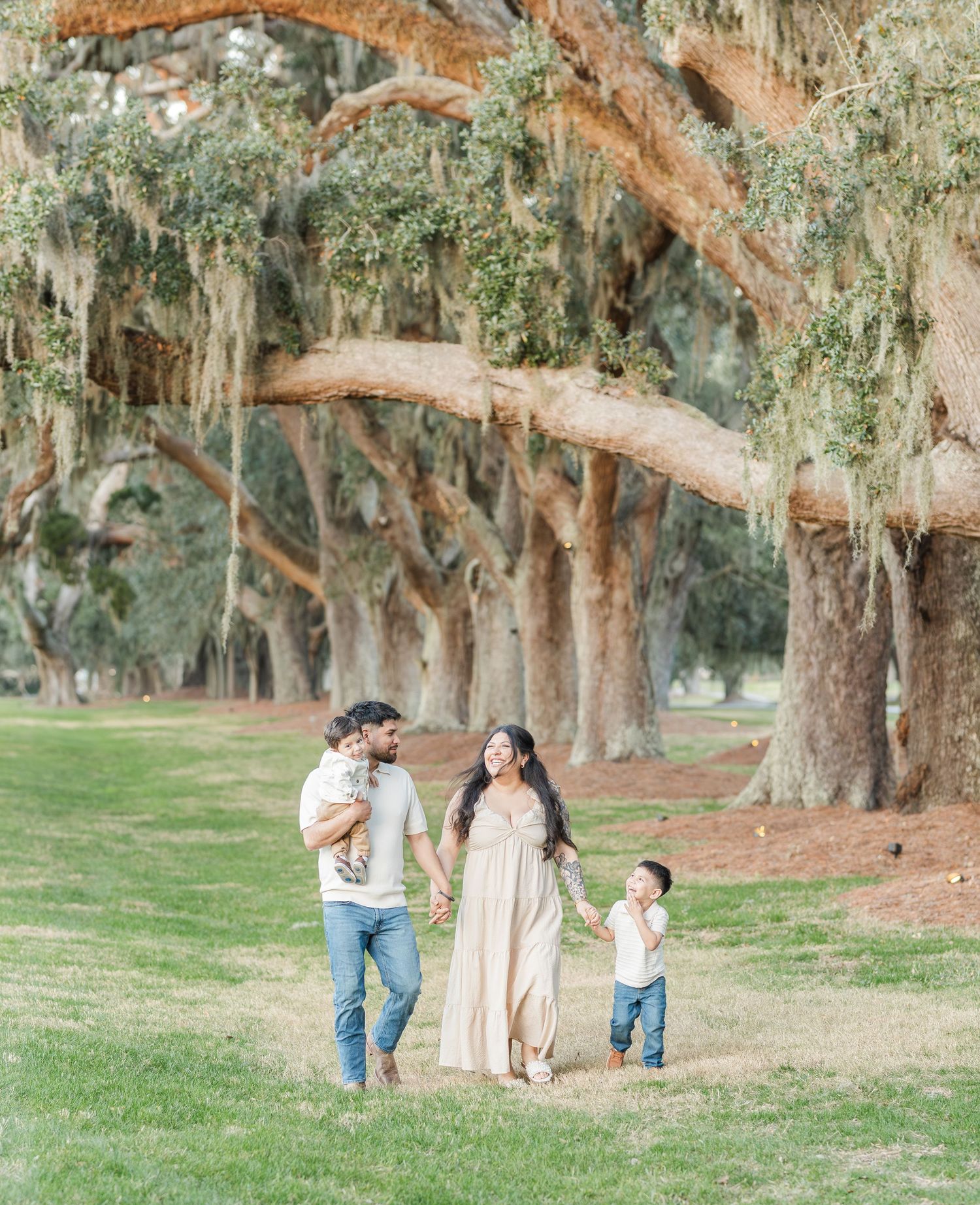 A family walks together beneath majestic oak trees draped with Spanish moss.
