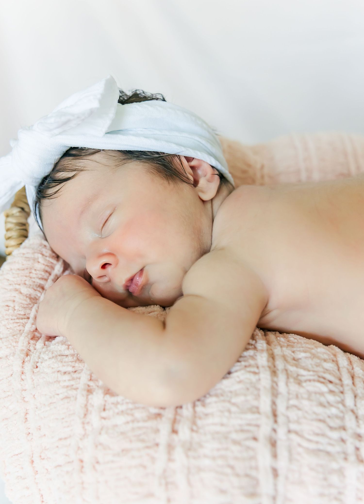 Sleeping infant wearing white headband rests on textured pink blanket.