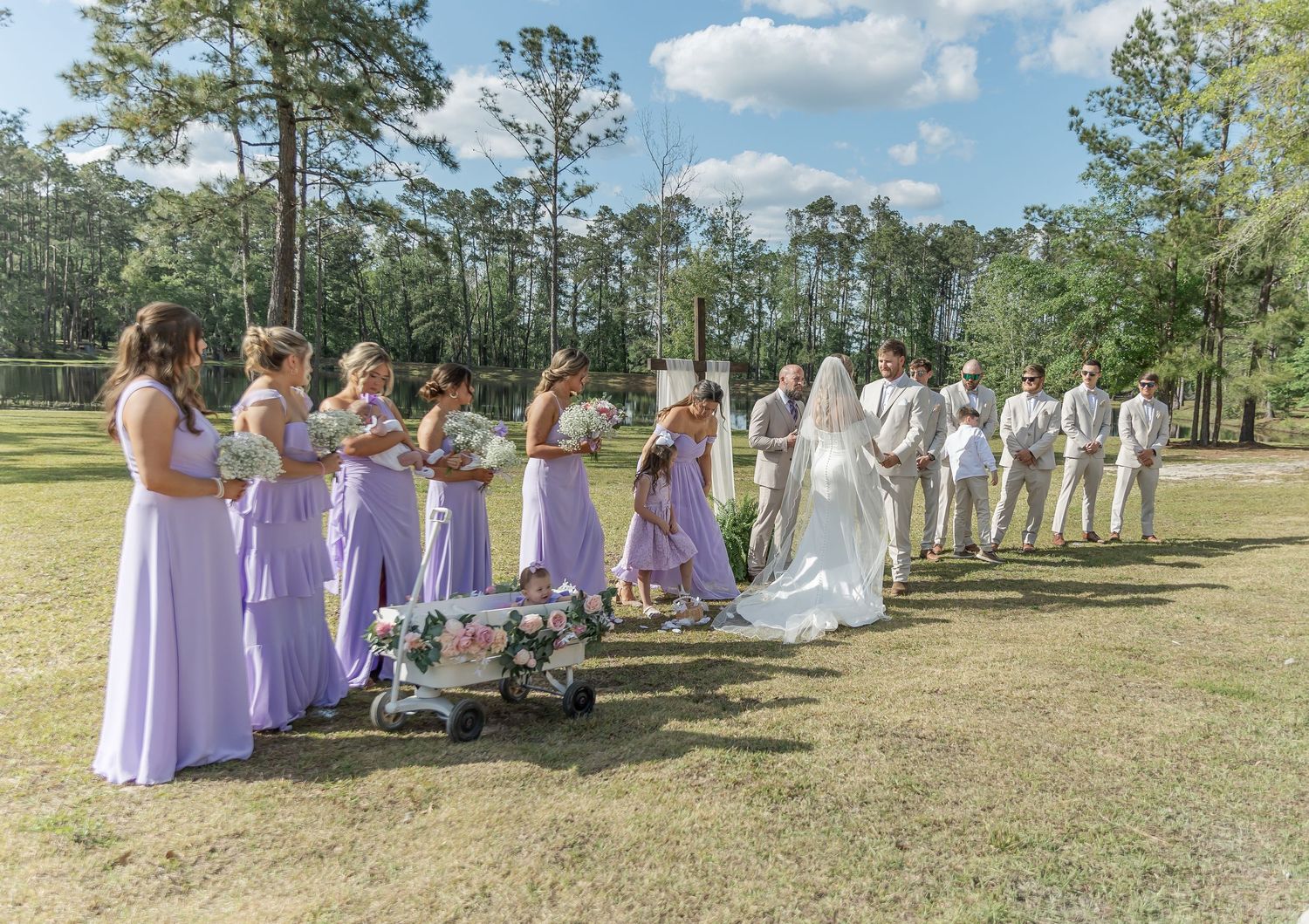 Wedding party in lavender dresses and light suits lined up for outdoor ceremony.