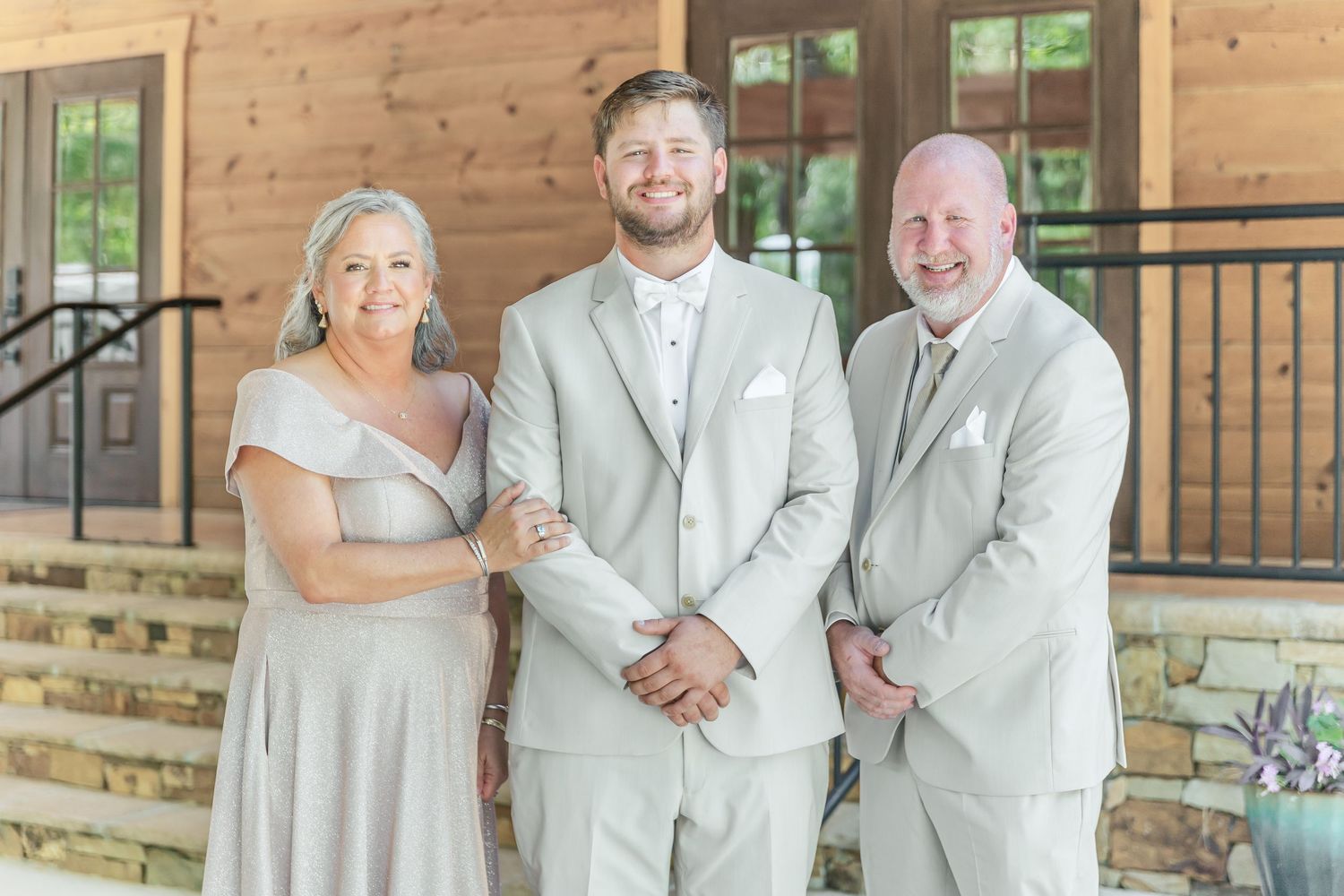 Three people in coordinated formal grey and white attire pose on wooden porch steps.