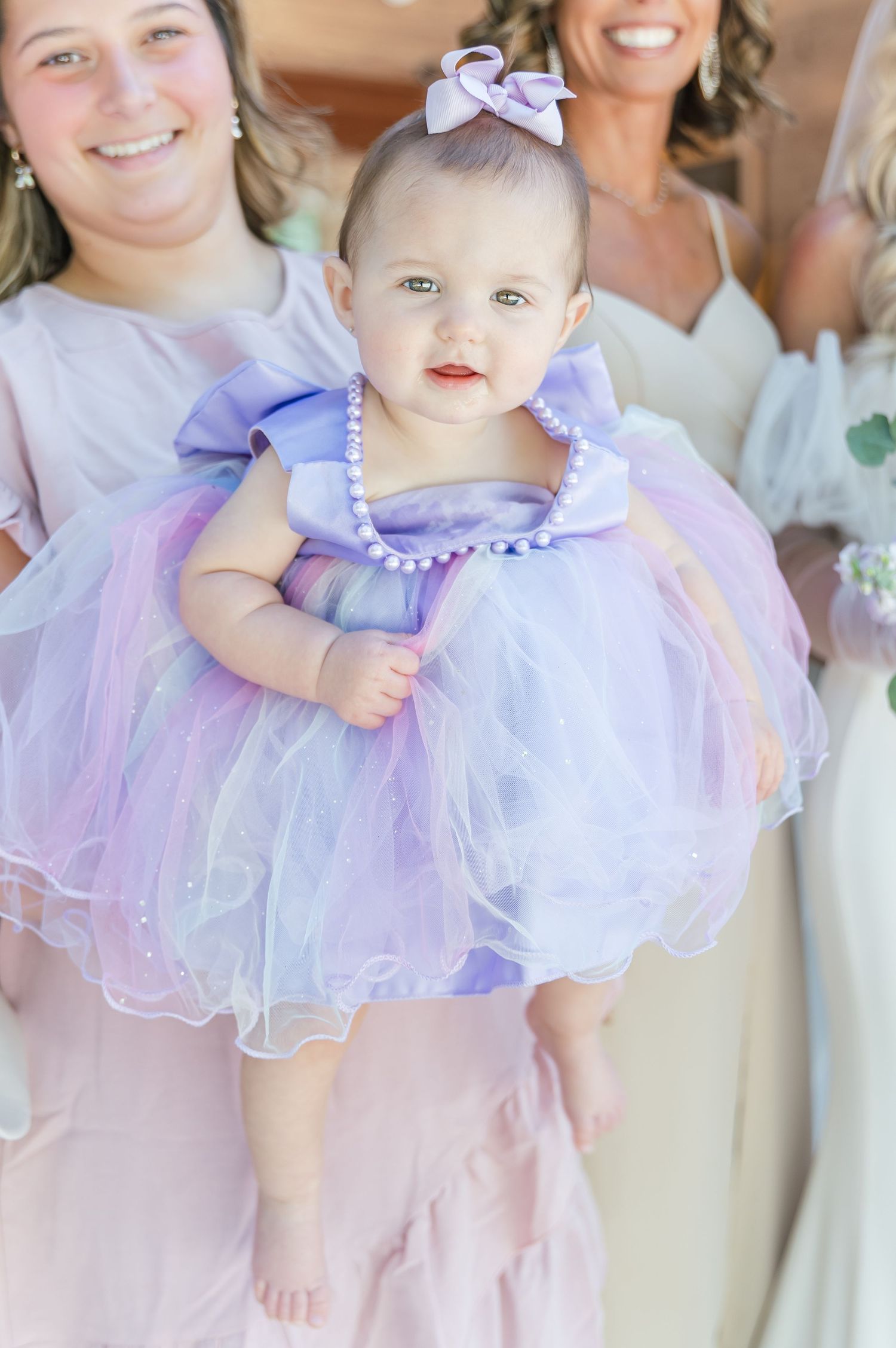 Baby in purple tulle dress with pearl details and bow at wedding.