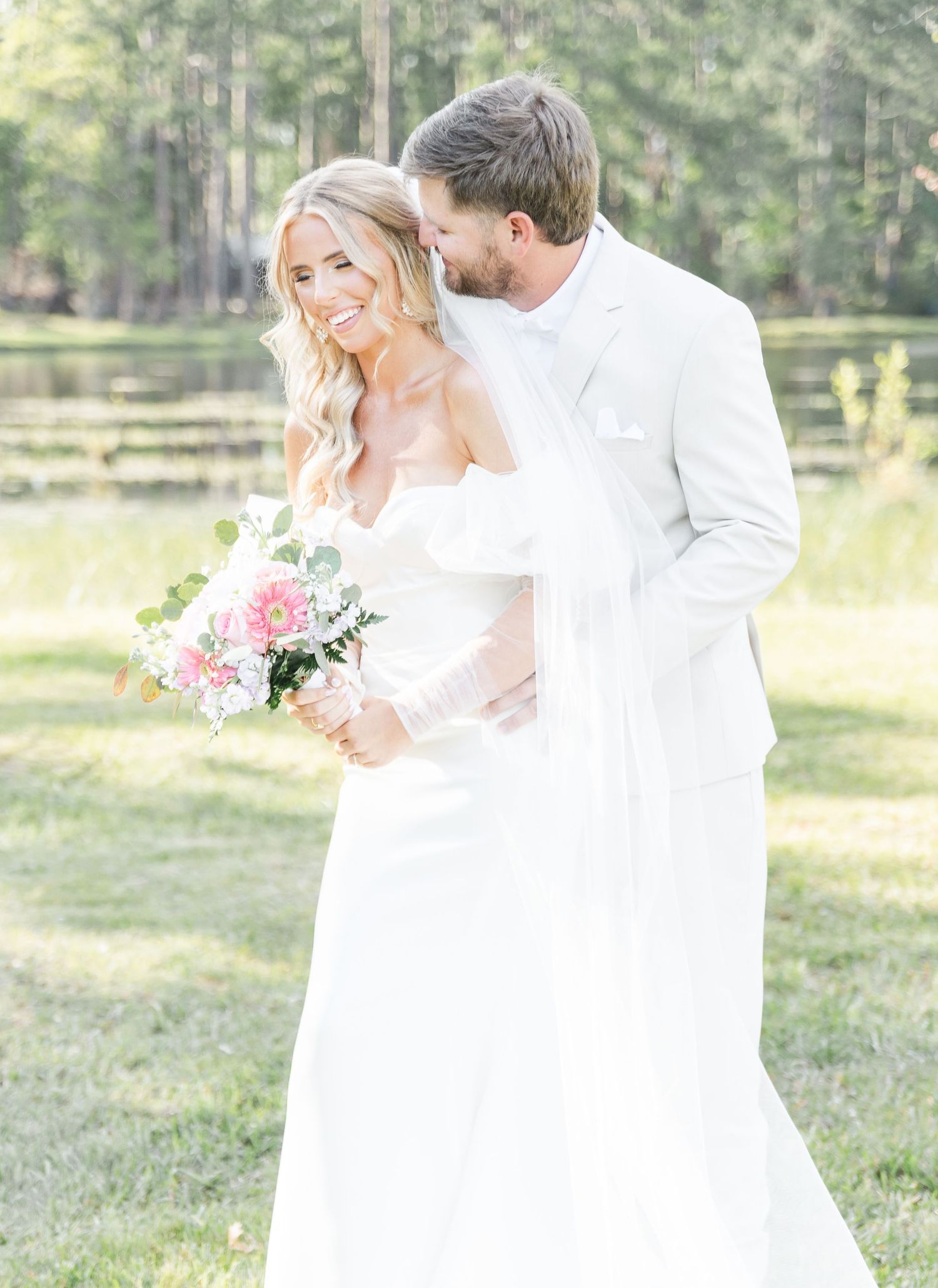 Dreamy wedding photograph of couple in white sharing tender moment in natural outdoor setting.