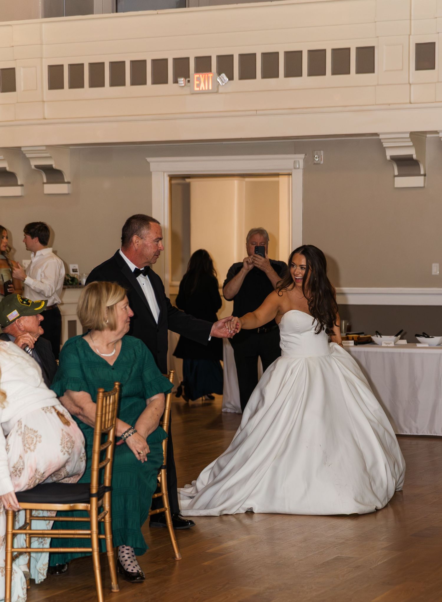 Bride in white ball gown shares a dance with a man in a tuxedo at an elegant wedding reception.