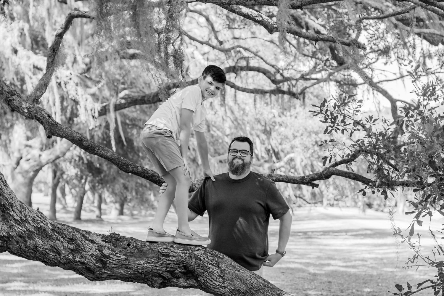 Two people interact on a curved tree branch in a black and white nature setting.